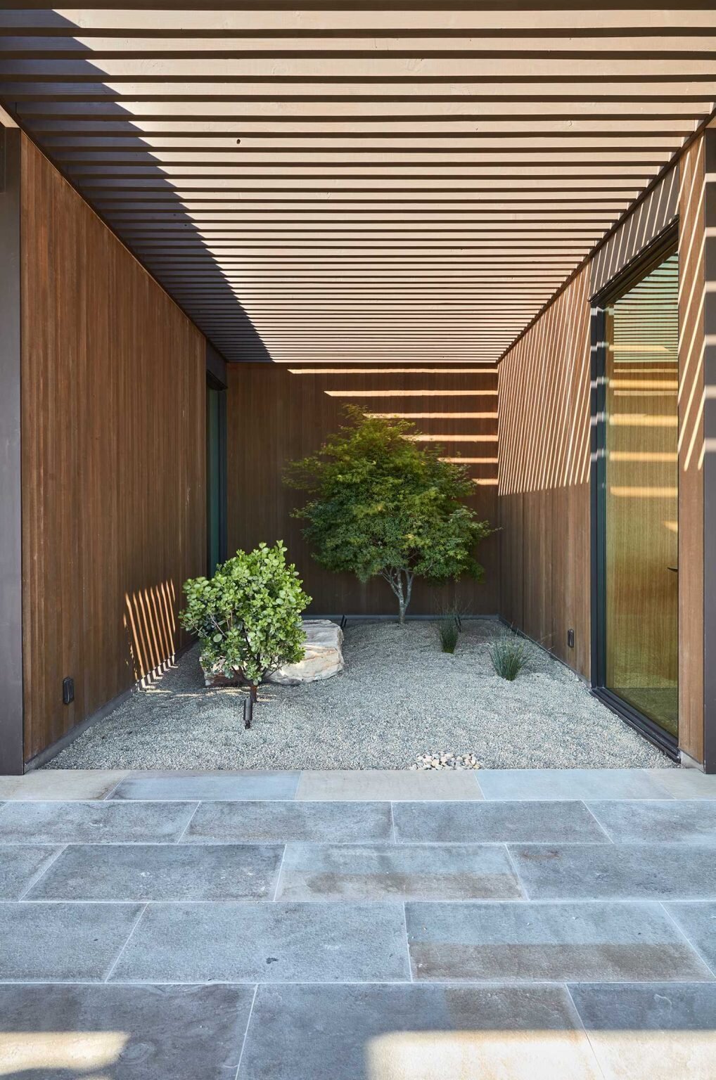Large glass openings connect the interiors to an expansive covered patio designed for dining, lounging, and entertaining outdoors.