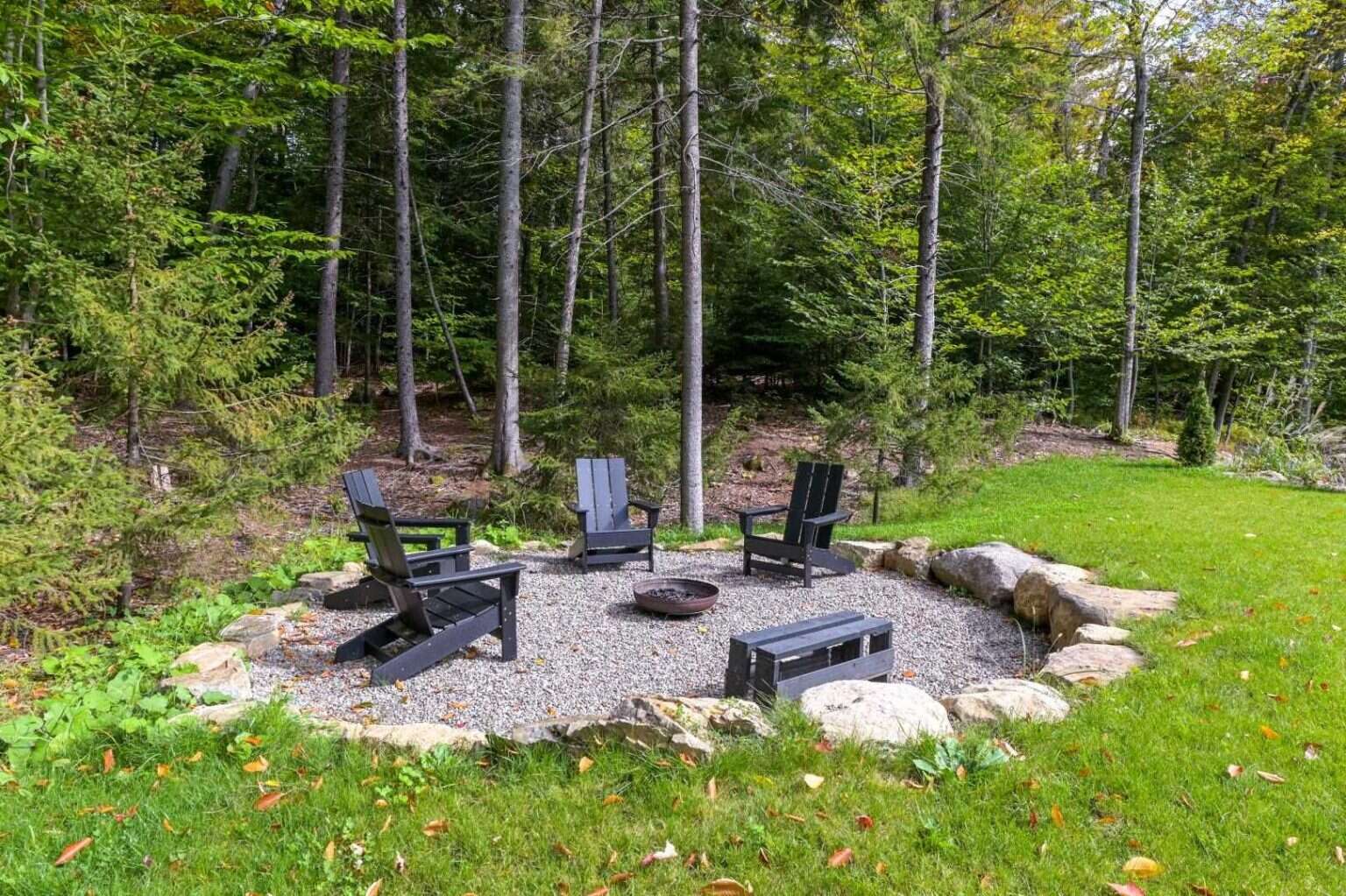 A stone firepit surrounded by seating creates the perfect outdoor gathering space in this forested Quebec setting.