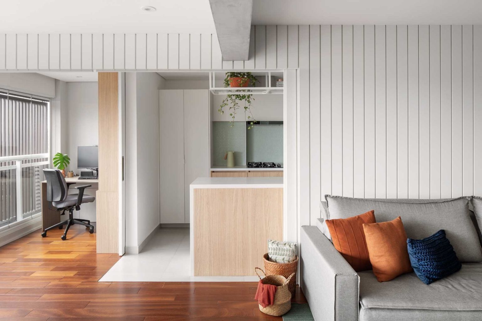 Discover how a striking white feature wall transforms this São Paulo apartment, hiding a home office and kitchen behind sleek sliding pocket doors while maintaining a clean, modern look.