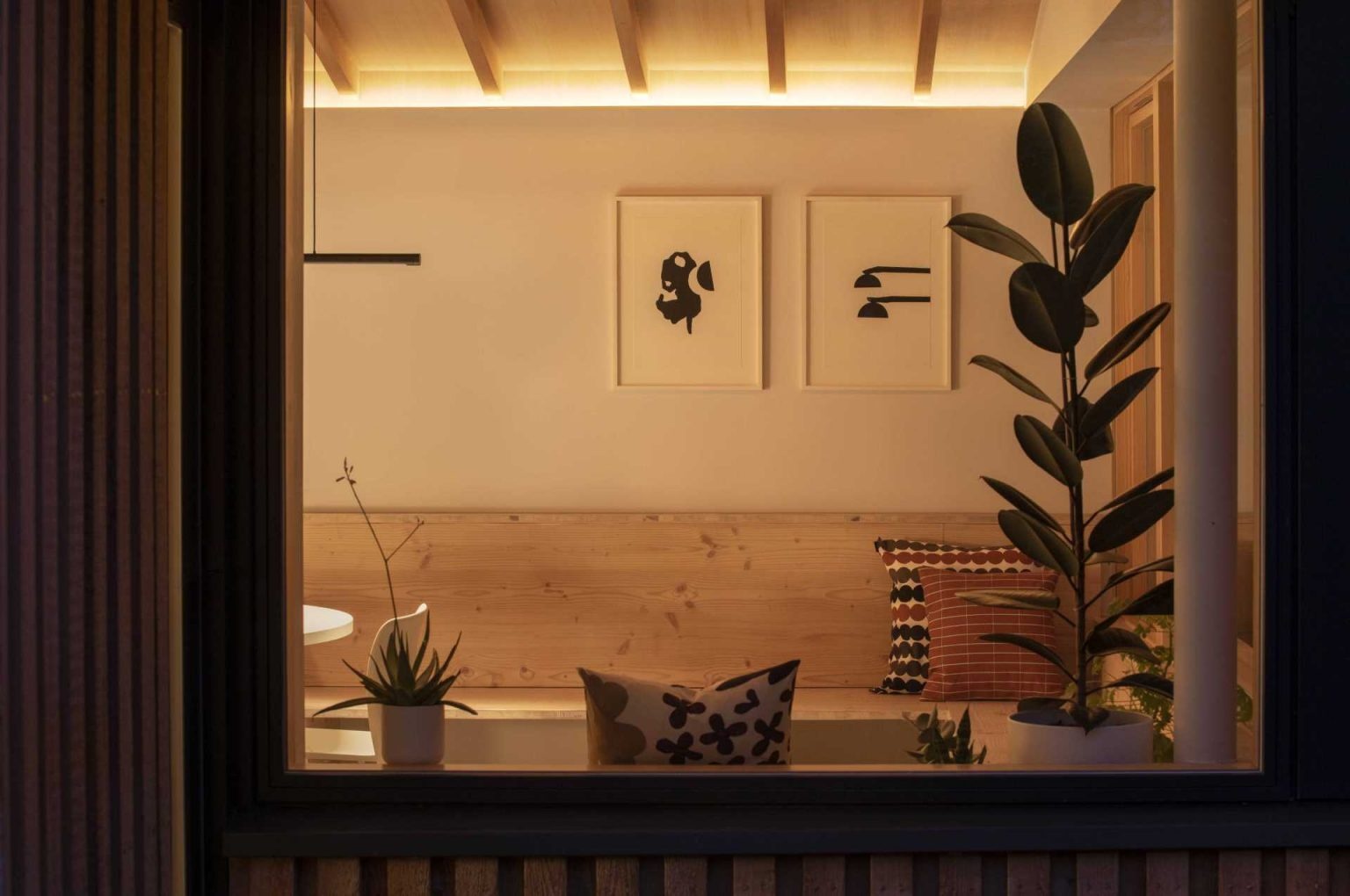 As night falls, interior lighting highlights the exposed timber ceiling, creating a warm glow throughout the extension. Viewed from the garden, the illuminated space showcases the beauty of the wood structure and welcoming atmosphere.
