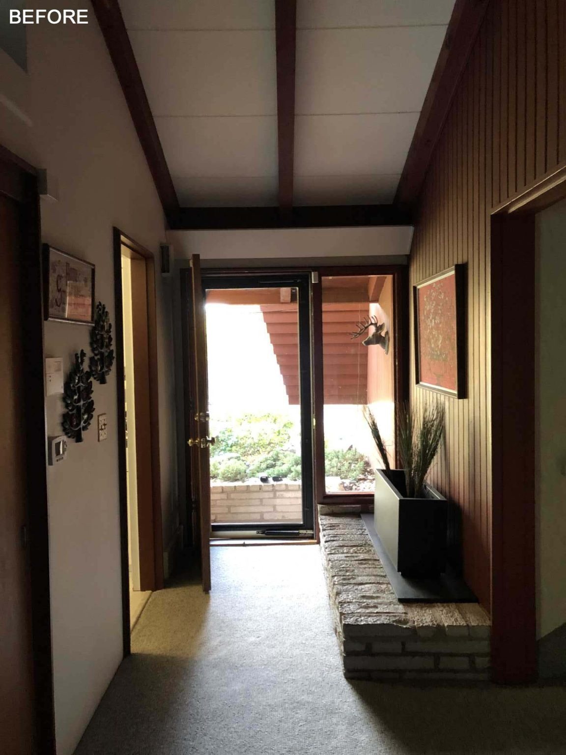 BEFORE - See how a dark mid-century entryway was transformed with light wood floors, grey finishes, and a large round mirror, while an original brick planter remains as a nod to the home's history.