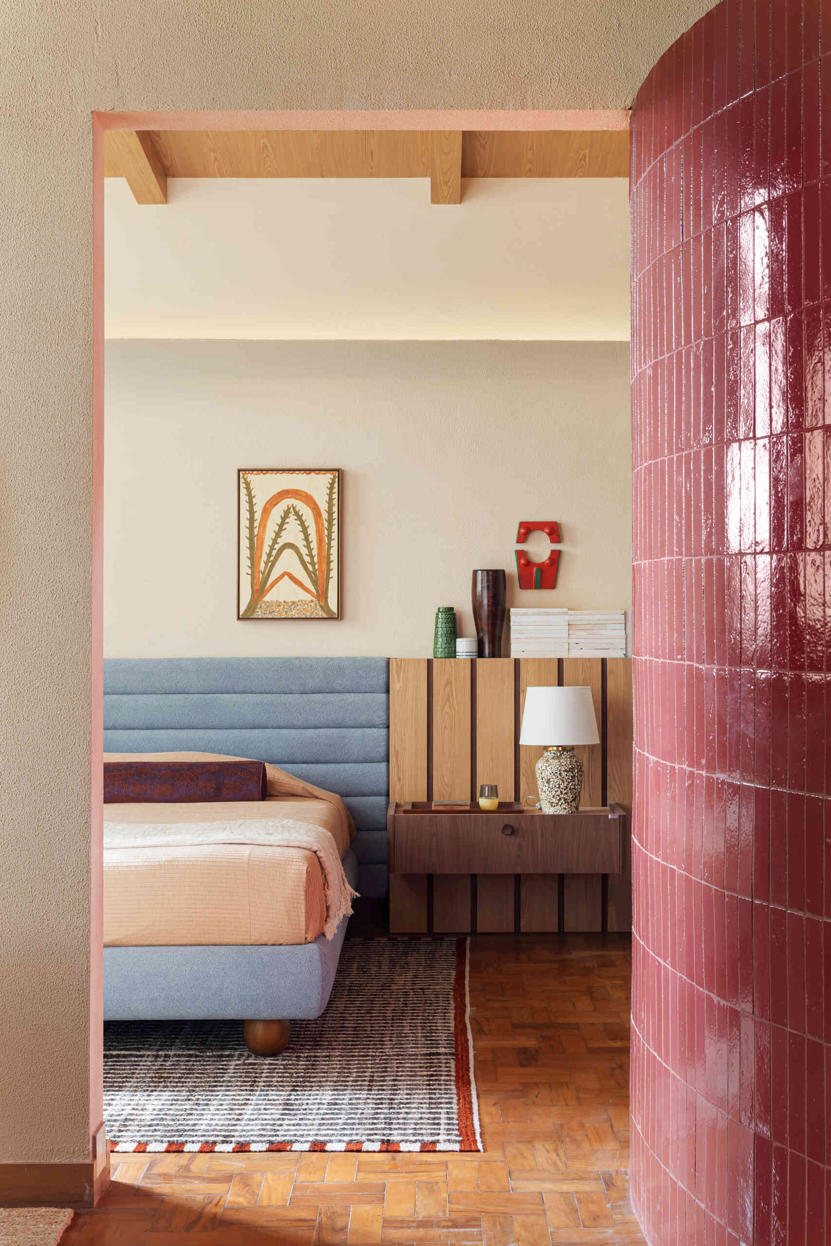 A blue upholstered headboard, slatted timber detailing, vintage lighting, and exposed beams create a serene bedroom full of character.