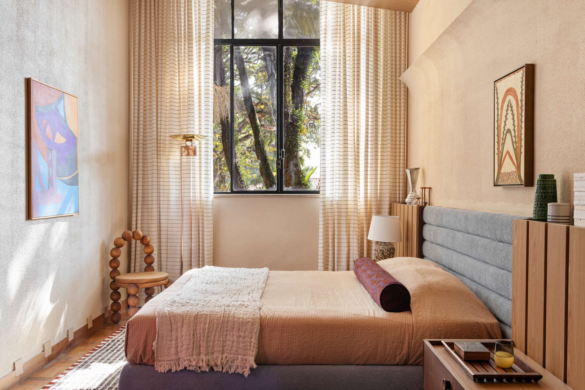 A blue upholstered headboard, slatted timber detailing, vintage lighting, and exposed beams create a serene bedroom full of character.