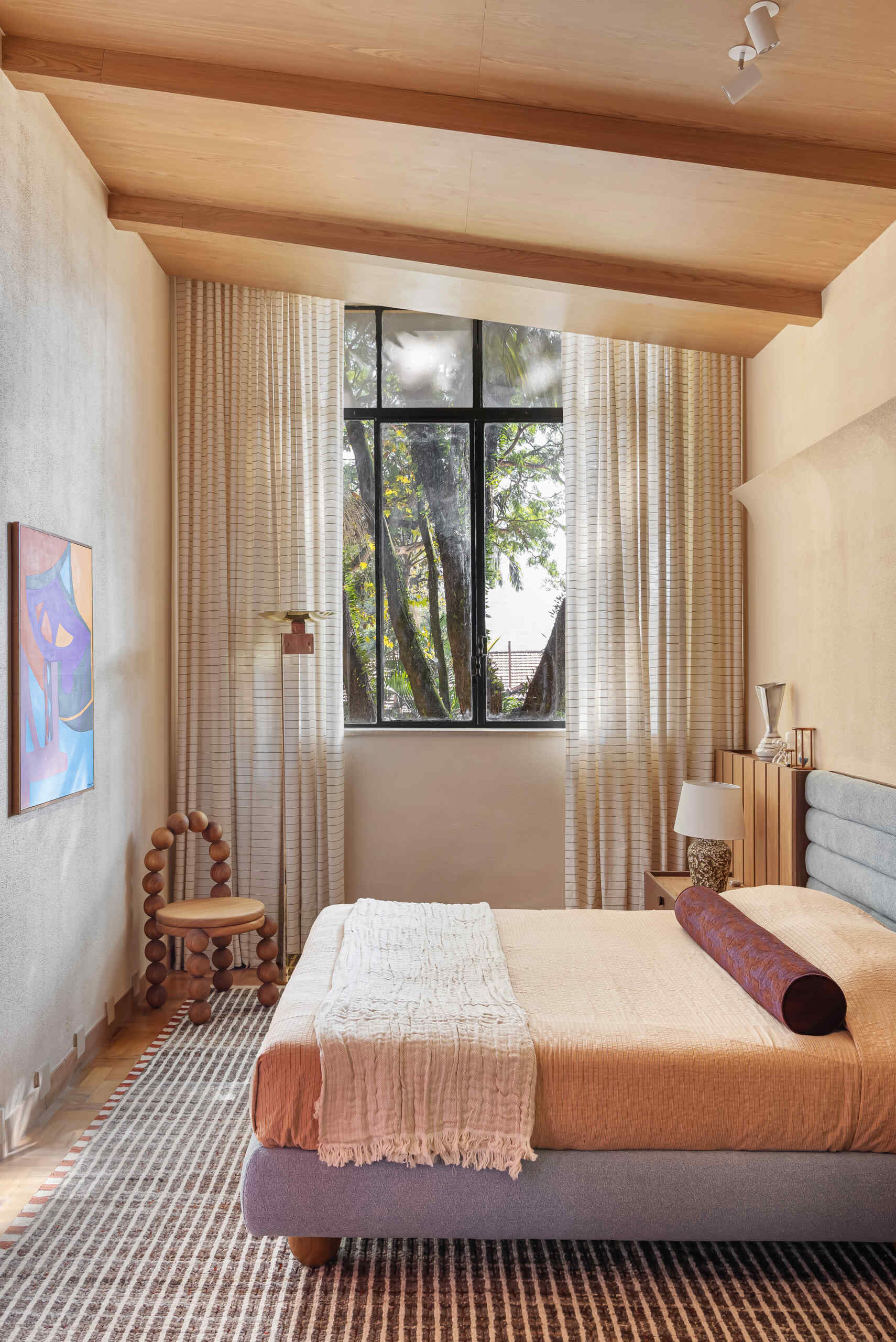 A blue upholstered headboard, slatted timber detailing, vintage lighting, and exposed beams create a serene bedroom full of character.