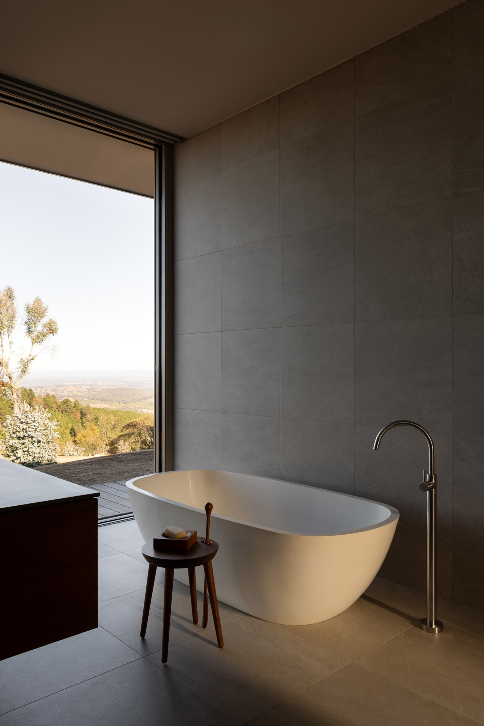 The ensuite bathroom extends the material palette found throughout the residence, combining stone, concrete, and eye-catching views from the bathtub.