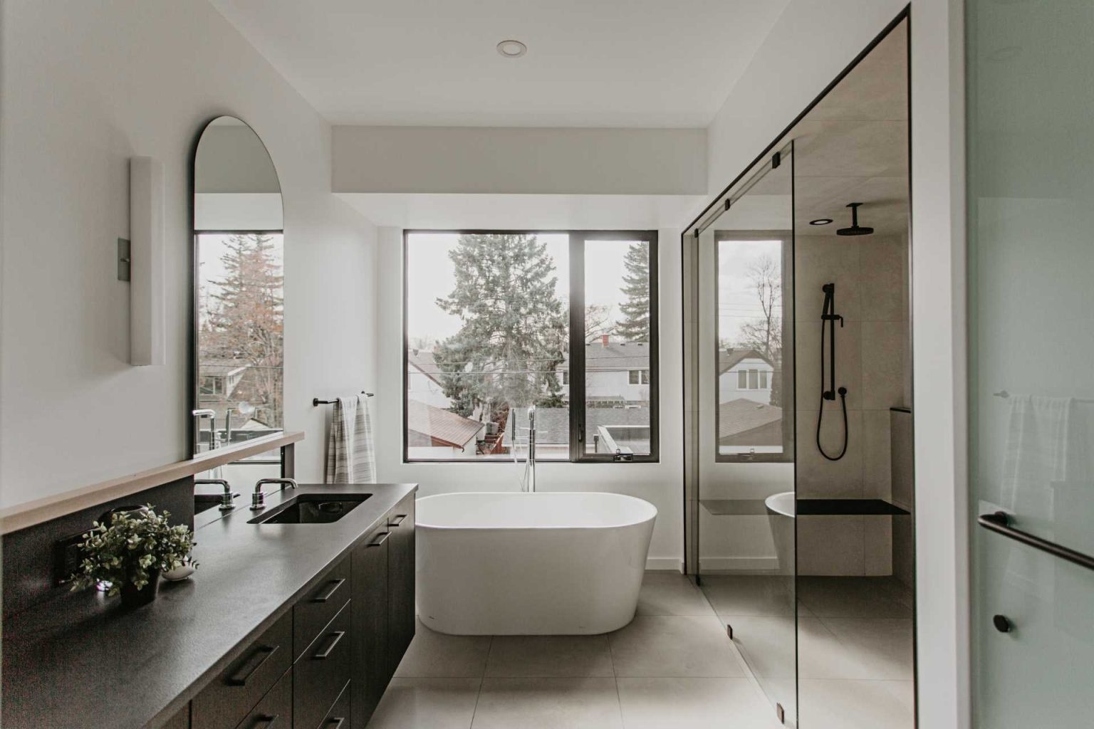 Arched mirrors, black vanities, terrazzo tile, and a freestanding tub create a bathroom full of elegant modern inspiration.