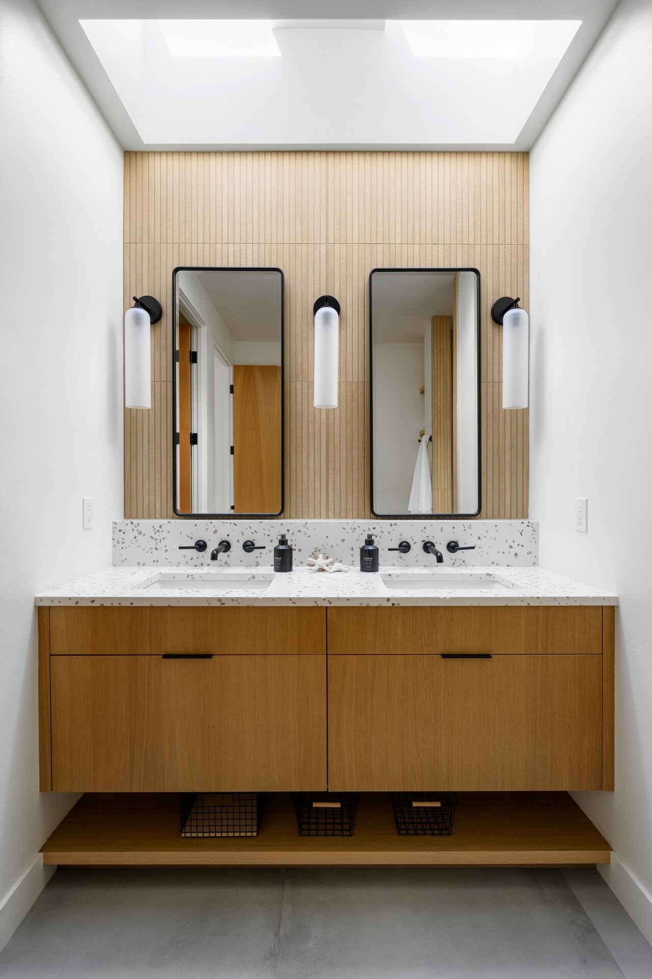 Discover a bright modern bathroom featuring warm timber cabinetry, skylights, black accents, and a beautifully cohesive material palette.