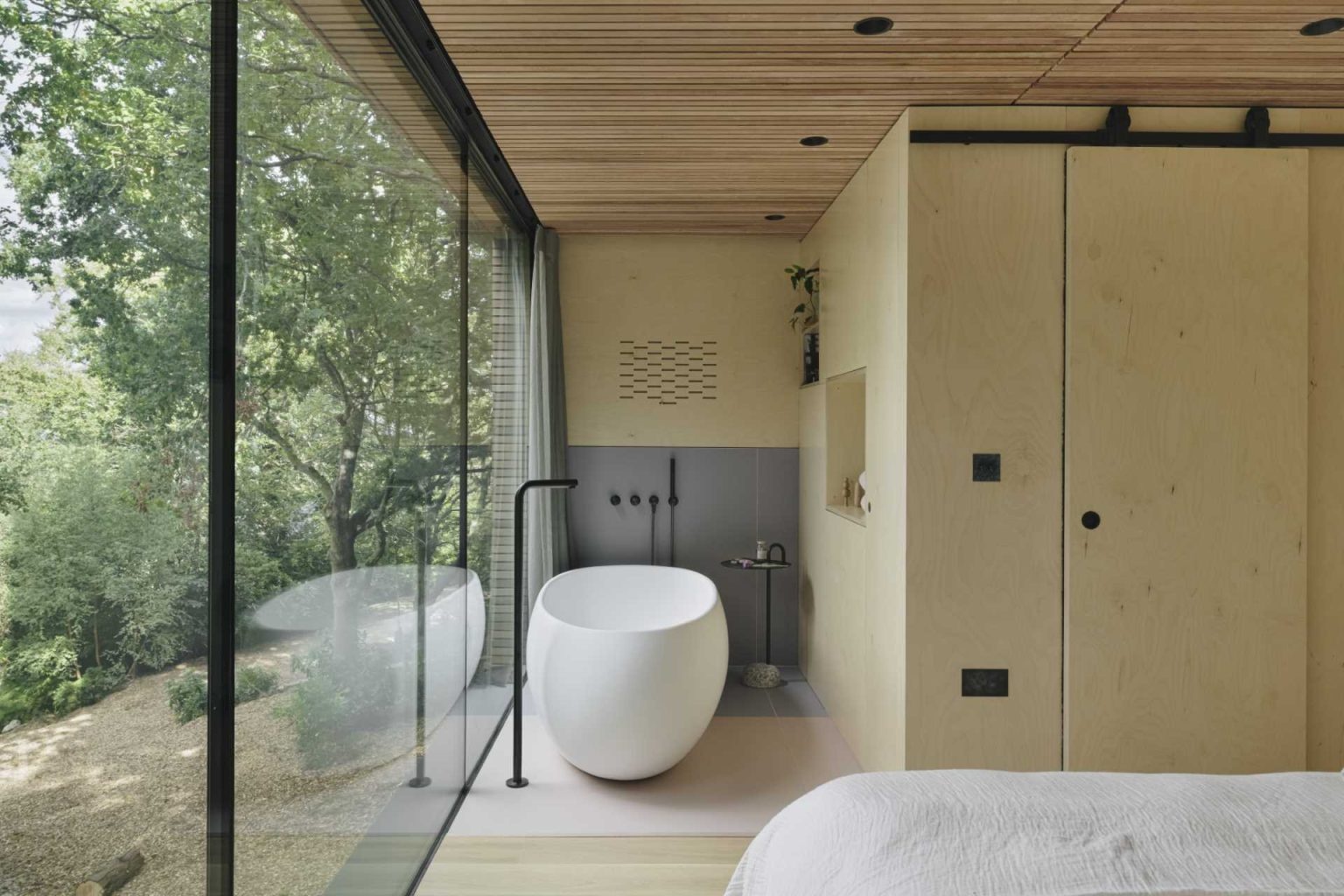 From a freestanding bathtub beside the windows to custom built-in shelving, this bedroom makes the surrounding woodland part of the interior experience.