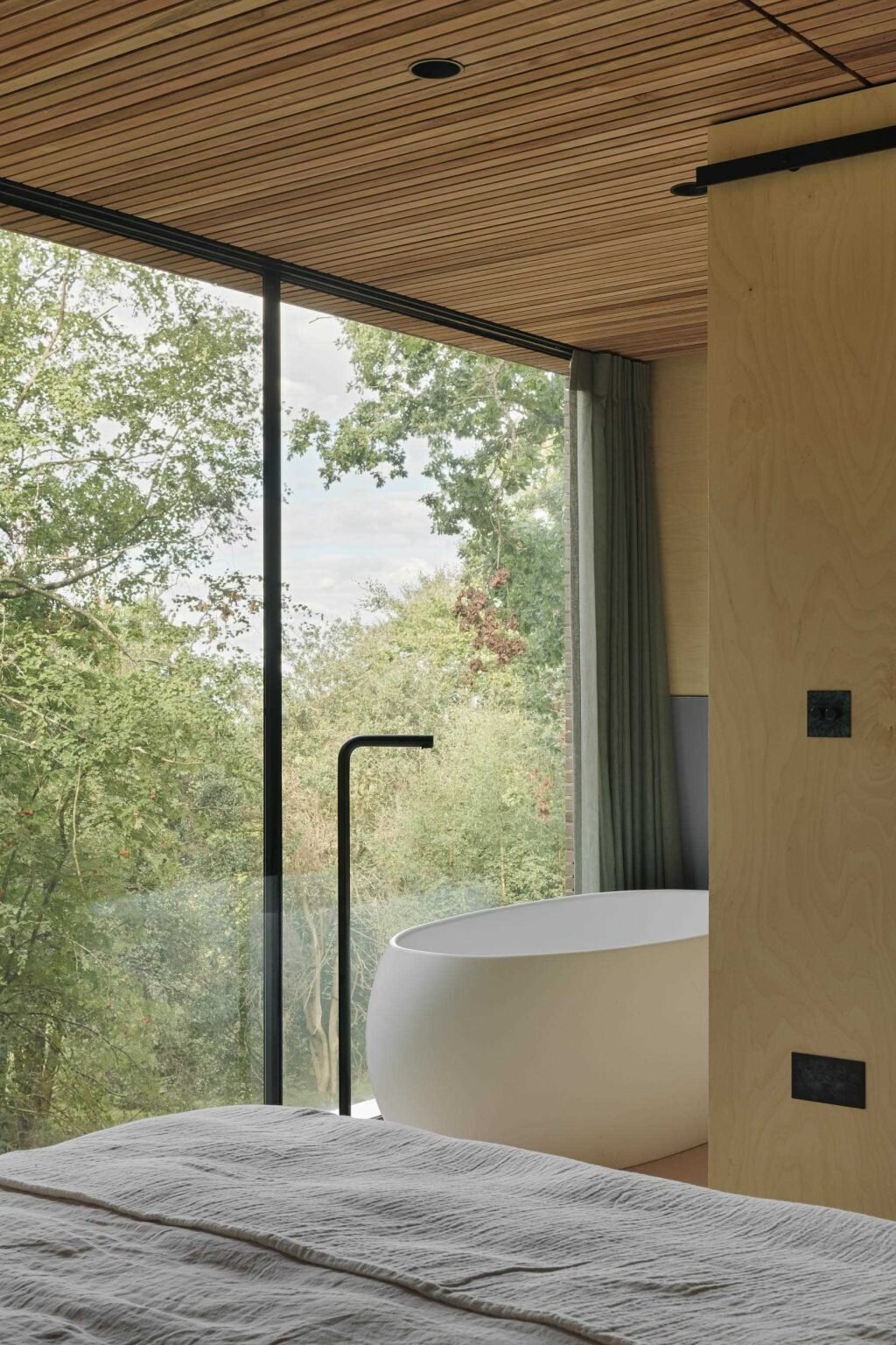 From a freestanding bathtub beside the windows to custom built-in shelving, this bedroom makes the surrounding woodland part of the interior experience.