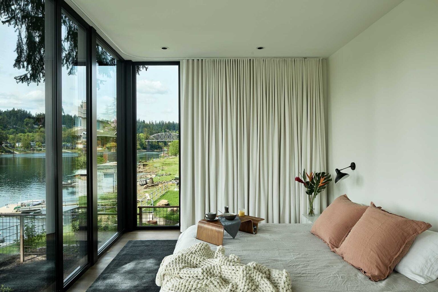 Floor-to-ceiling windows frame stunning river views in this modern bedroom, creating a bright and peaceful space.