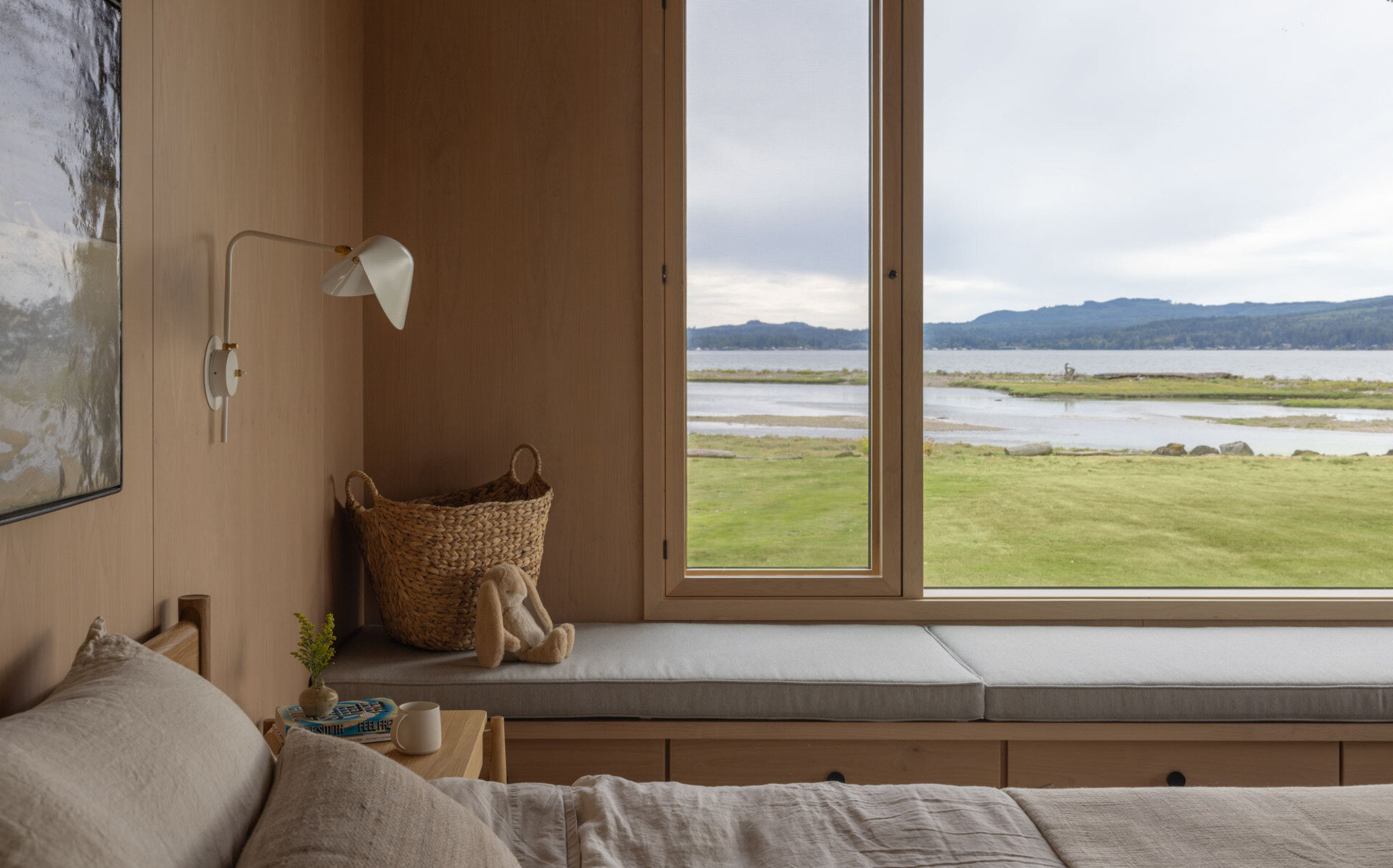 The main bedroom, with a built-in wraparound bench, enjoys a peaceful waterfront position with natural light and expansive views across Dyes Inlet.