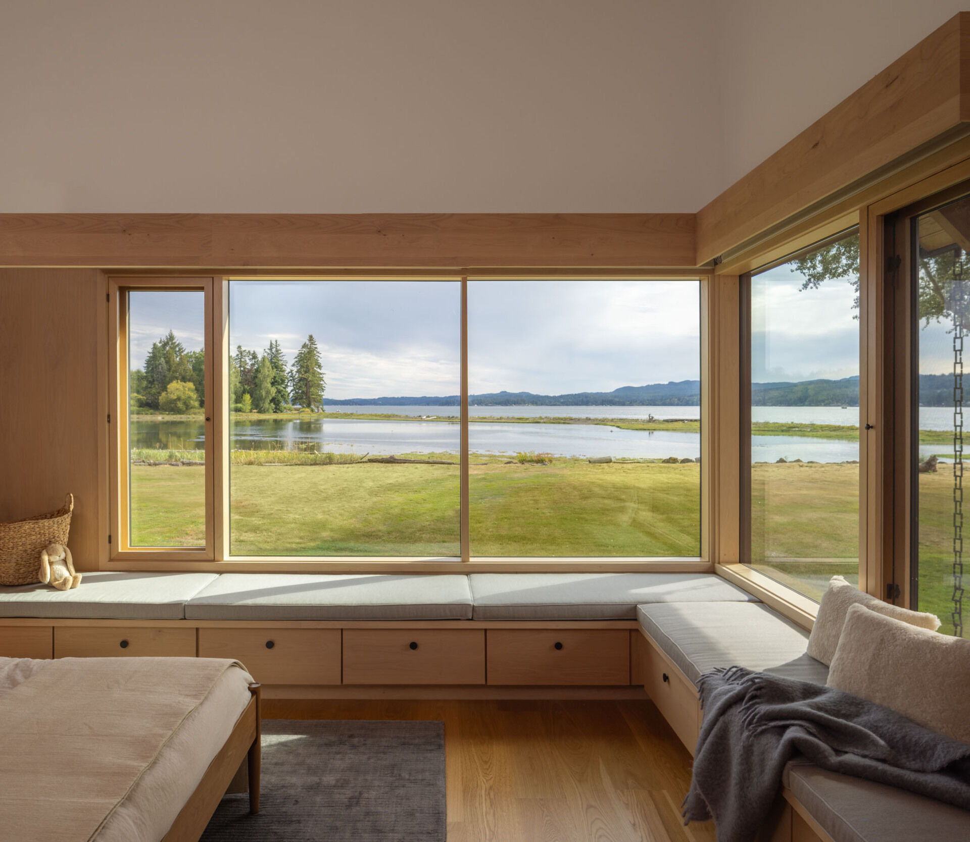 The main bedroom, with a built-in wraparound bench, enjoys a peaceful waterfront position with natural light and expansive views across Dyes Inlet.