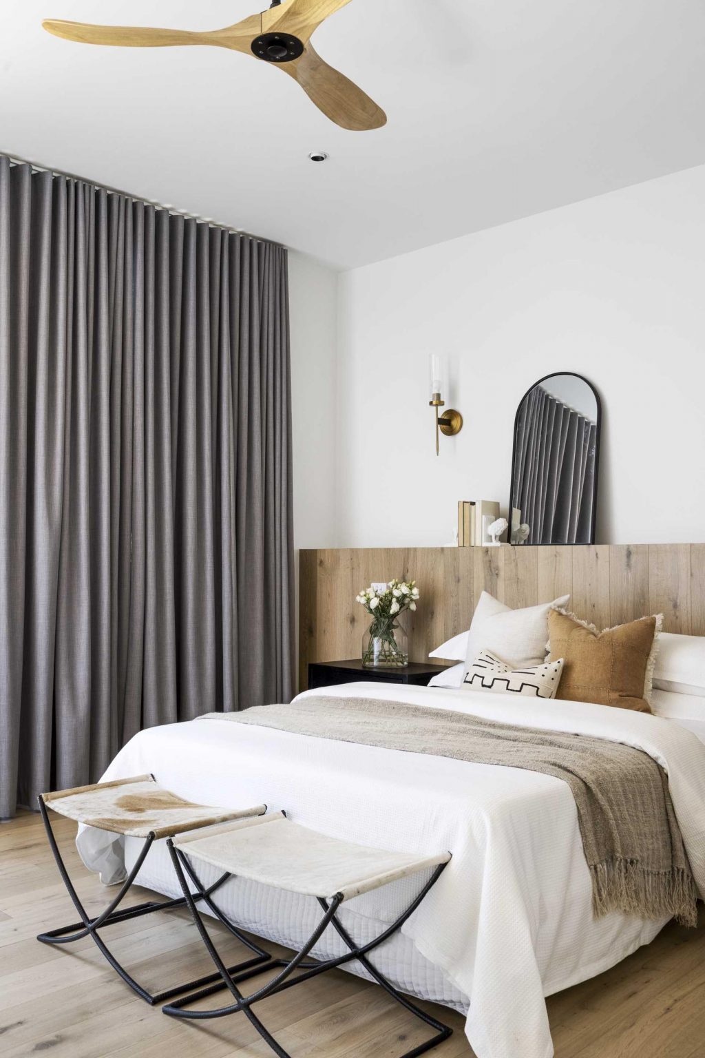 Heavy curtains, a full-width timber headboard, and simple finishes create a bedroom designed for comfort and relaxation.