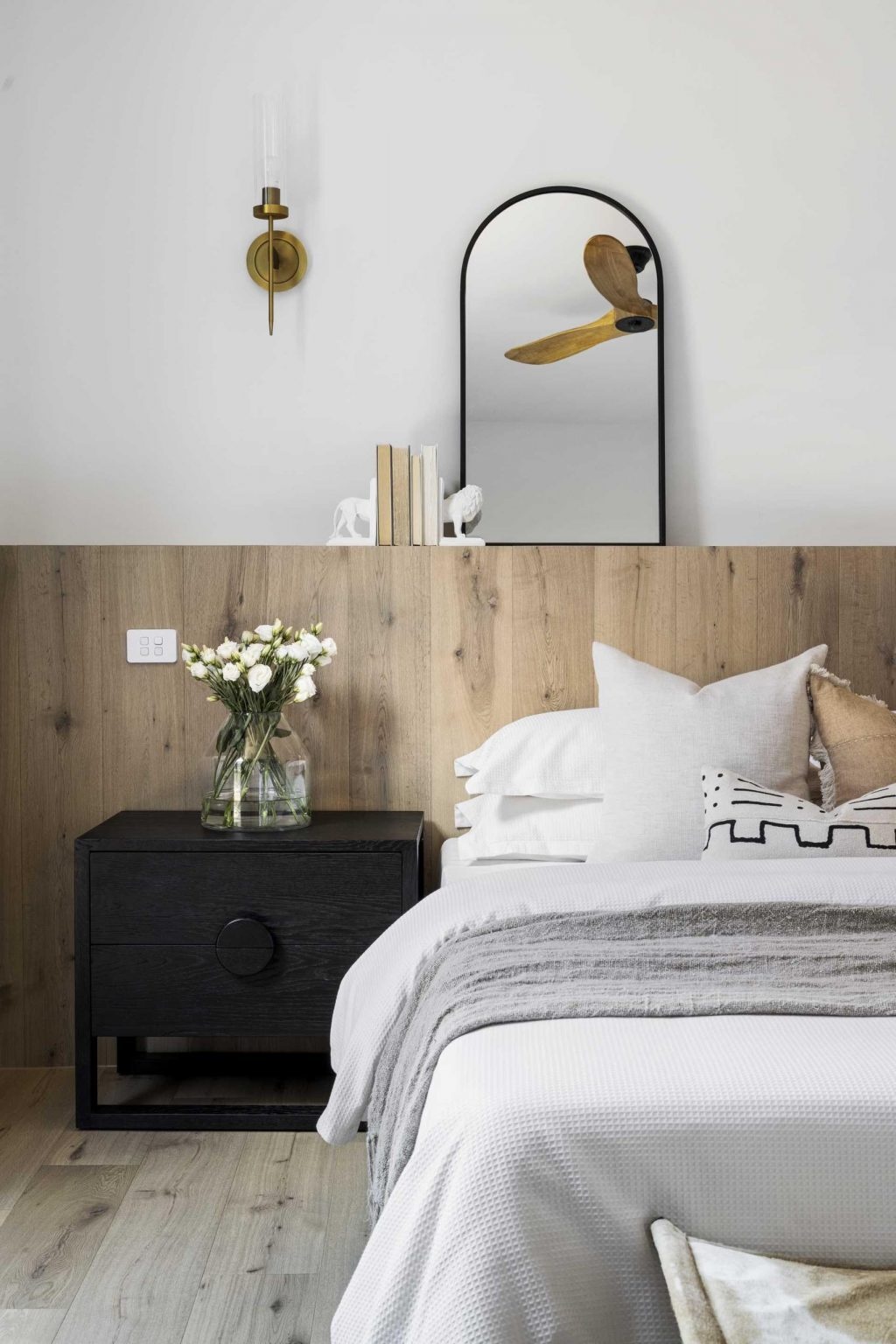 Heavy curtains, a full-width timber headboard, and simple finishes create a bedroom designed for comfort and relaxation.
