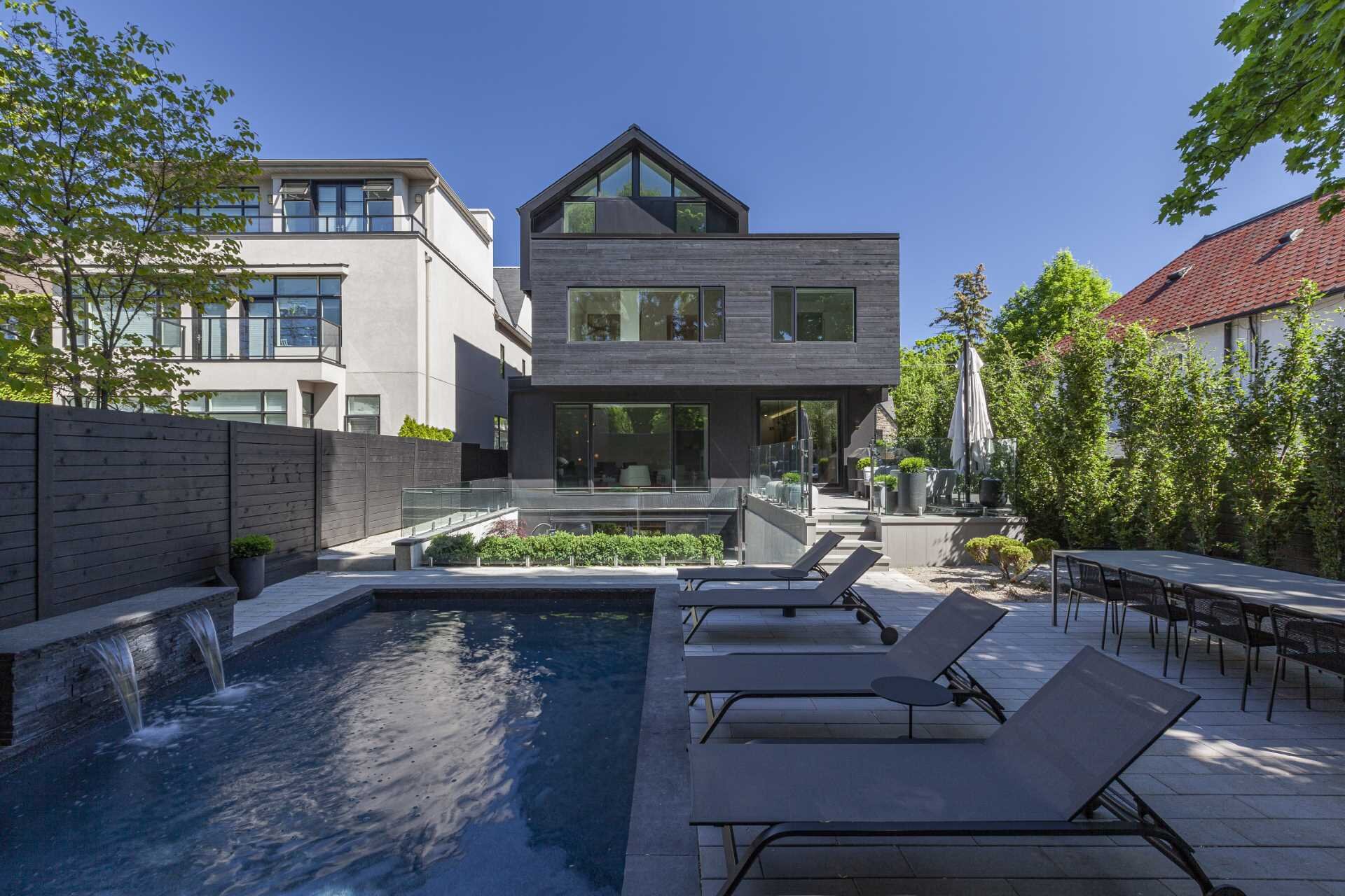 The backyard of Stack House features a swimming pool, outdoor dining area, patio, and terraced garden with weathered steel planters. A layered landscape design complements the bold architecture.