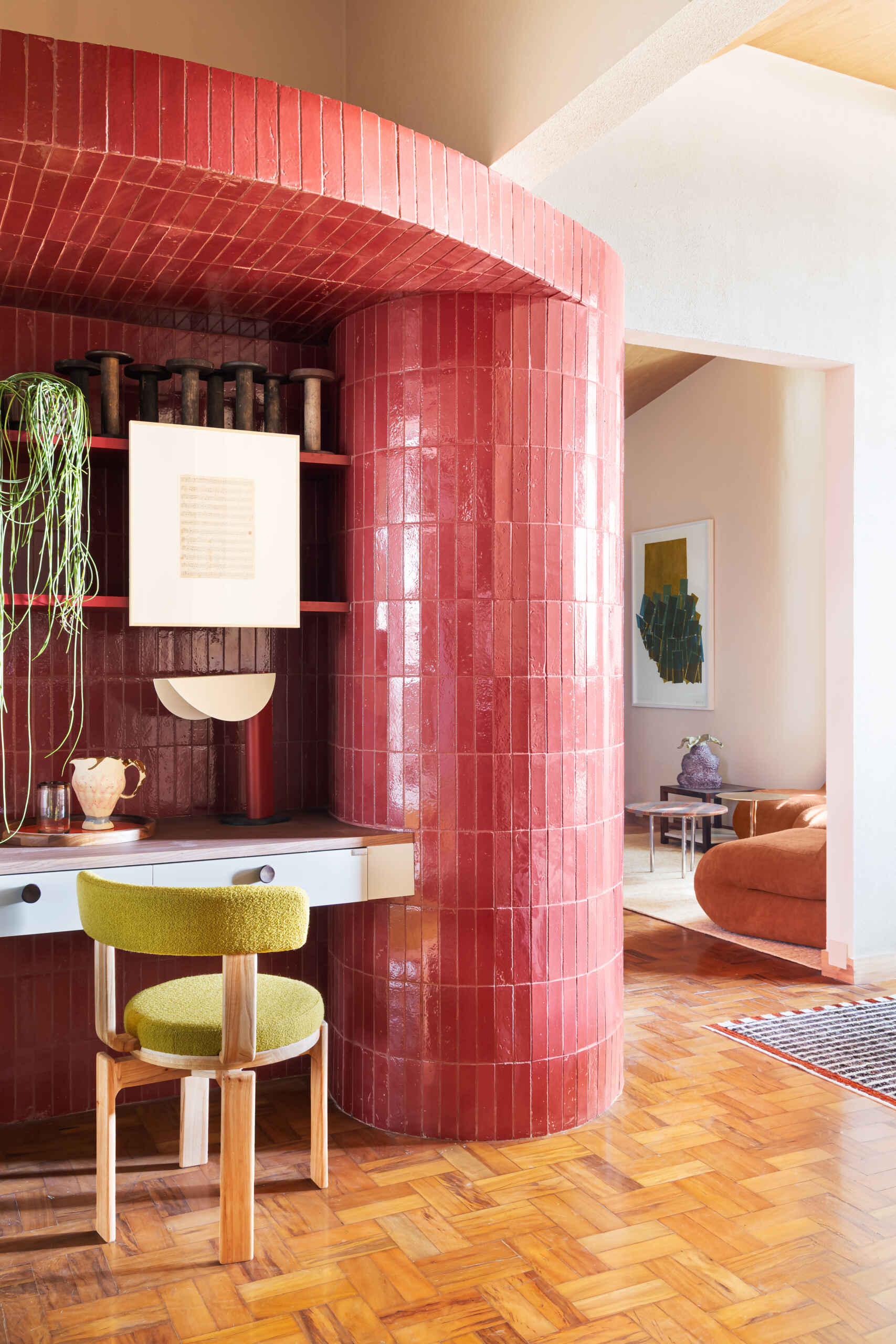 A striking burgundy-tiled cylinder becomes the defining architectural feature of this compact studio, adding color, texture, and sculptural impact.