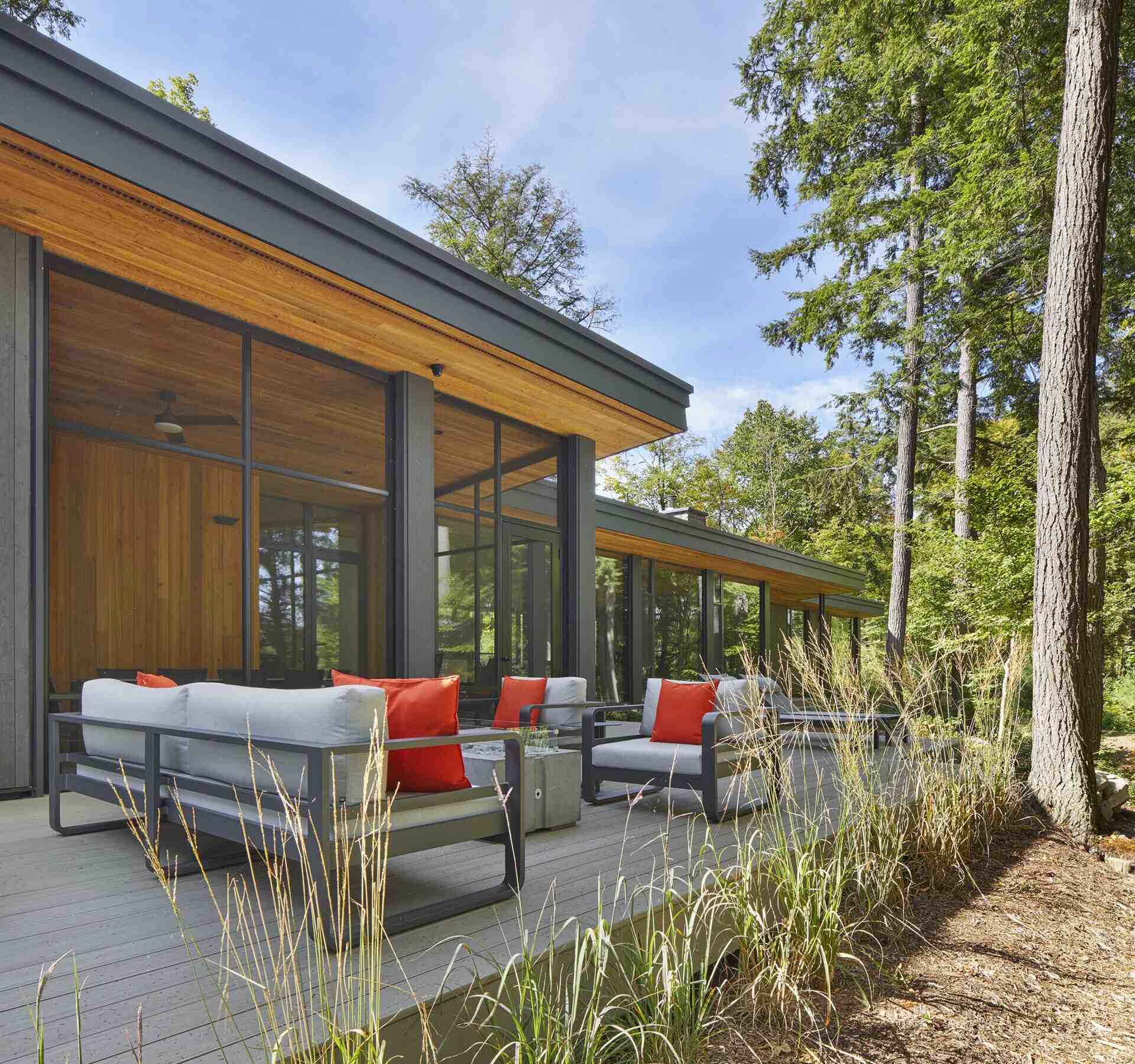 The deck, located off the screened porch, looks out towards the lake. Light gray outdoor furniture keeps the seating area soft and casual, with orange pillows adding just the right pop of color. Tall grasses along the edge help the deck settle into the landscape.