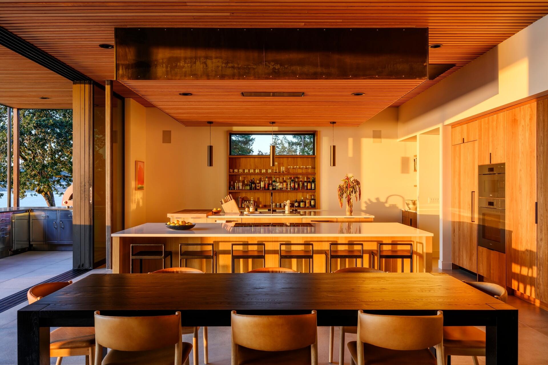 Discover a waterfront dining space where a long timber table, seamless indoor-outdoor living, and panoramic Puget Sound views create the perfect setting for entertaining.
