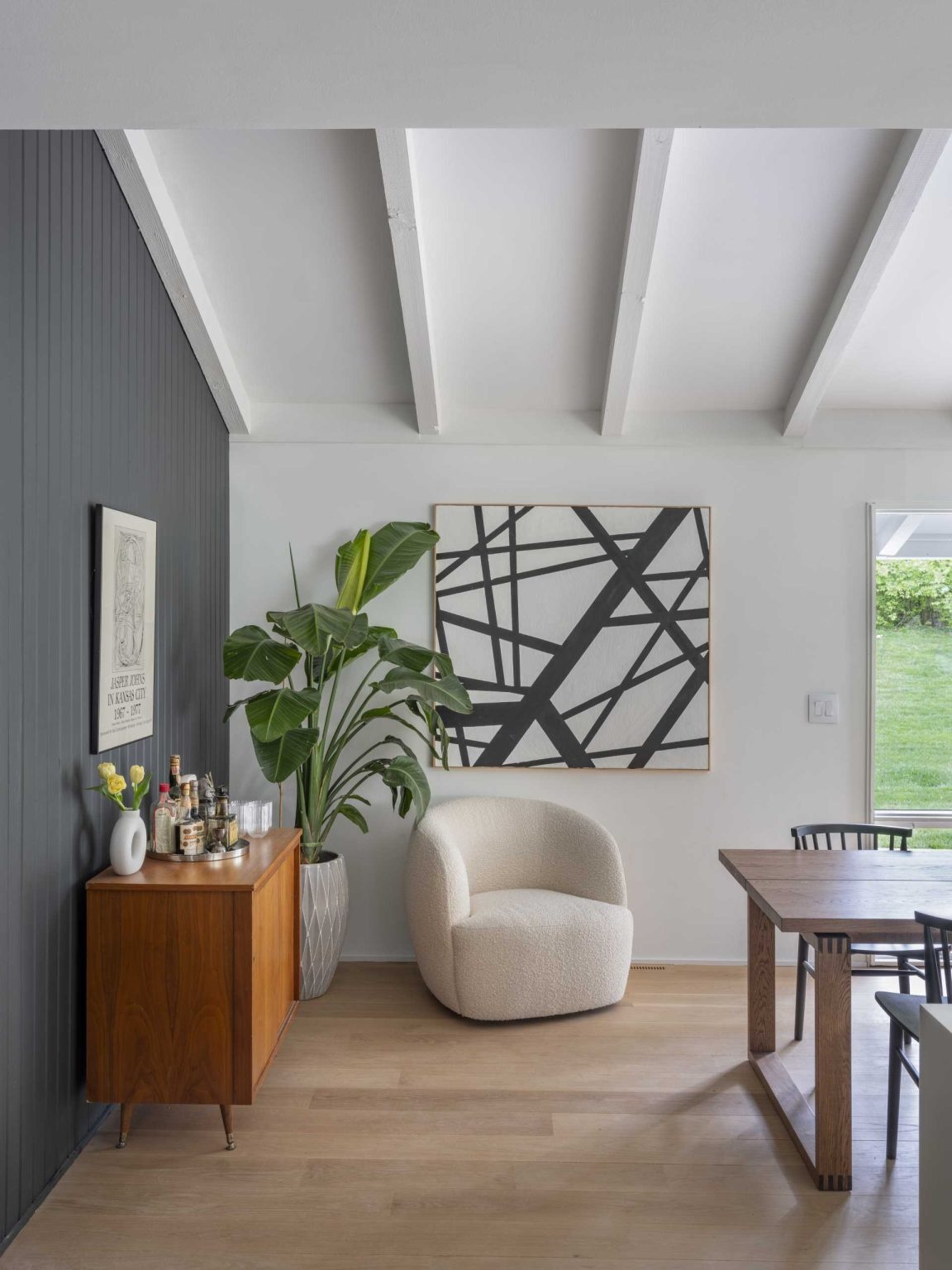 An original living room becomes a bright dining space centered around a preserved double-sided brick fireplace. Open views and mid-century furnishings help connect the home's updated interiors.