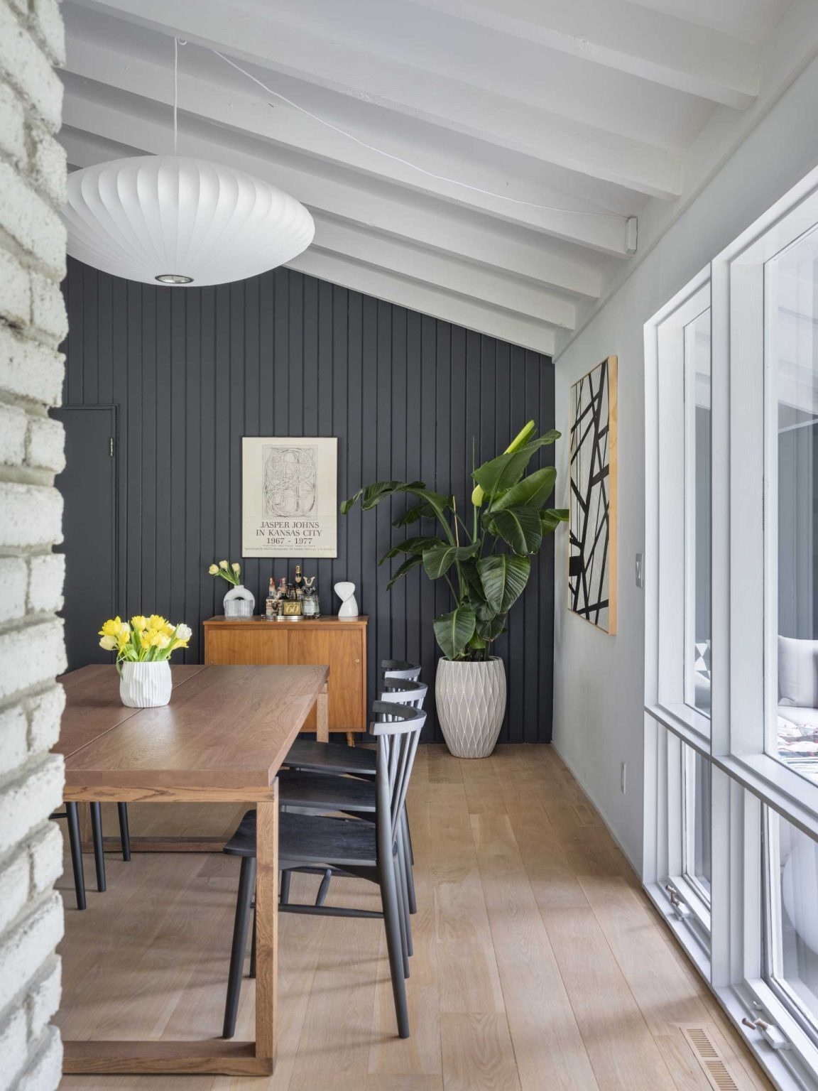 An original living room becomes a bright dining space centered around a preserved double-sided brick fireplace. Open views and mid-century furnishings help connect the home's updated interiors.