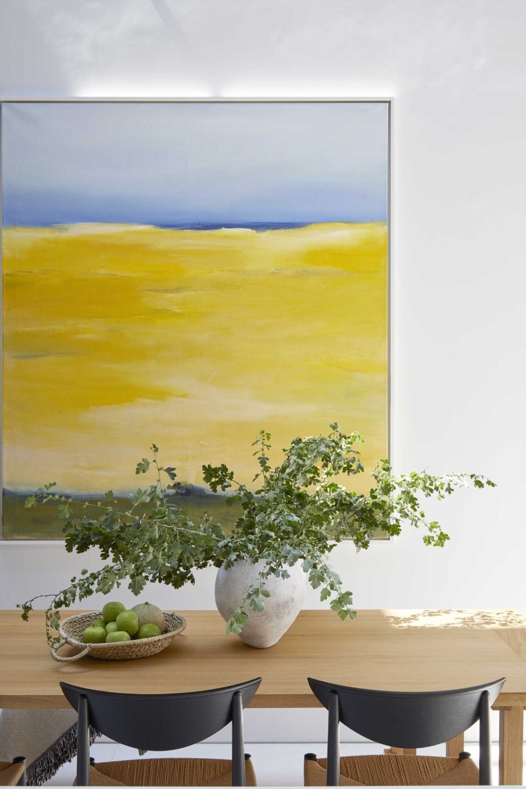 Warm timber furnishings, contemporary details, and colorful artwork create an inviting dining area beneath a skylight.