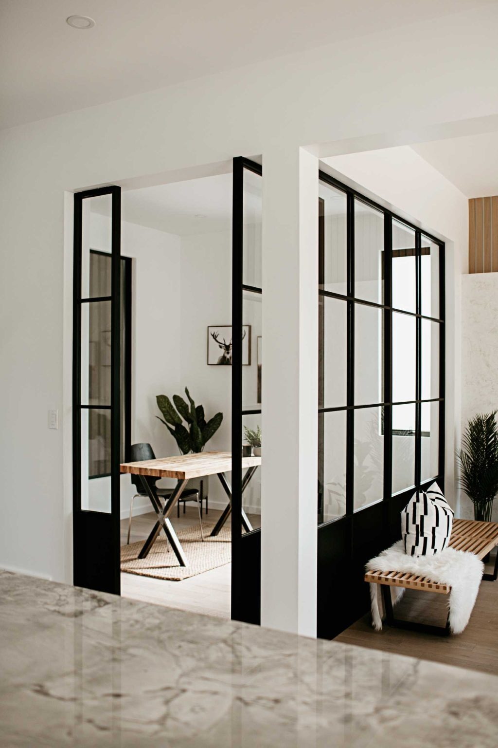Just off the kitchen, the home office is enclosed with thick black-framed windows and a pivoting glass door. The black framing echoes the kitchen cabinetry while allowing natural light to travel freely between rooms.
