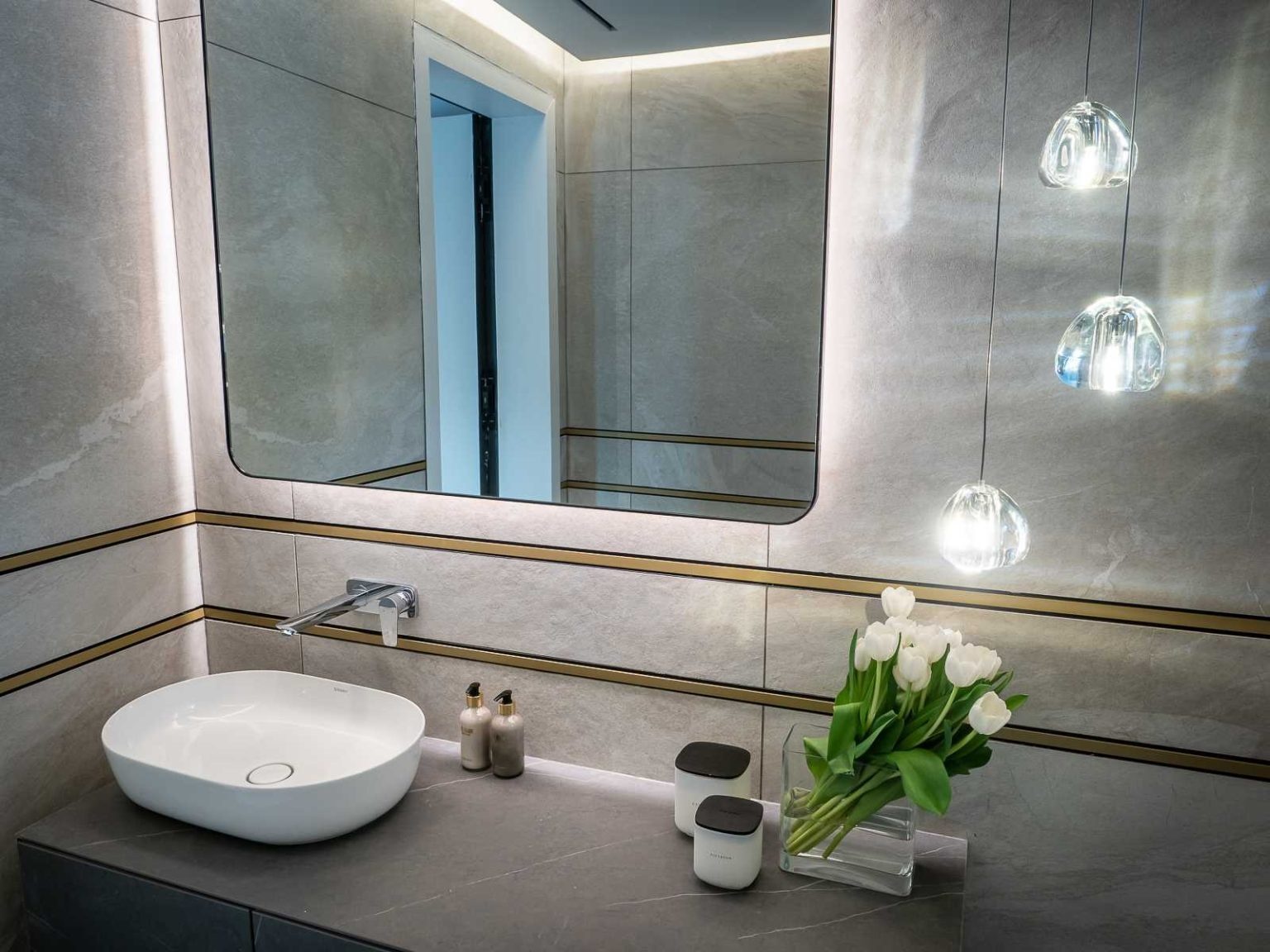 Integrated ceiling lighting in the primary bathroom and a backlit mirror in the guest bathroom add a refined touch to these contemporary spaces.