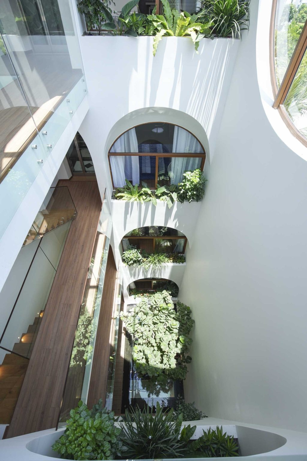 A dramatic central atrium filled with plants, bridges, skylights, and a koi pond brings natural light and greenery to every level of this Vietnam home.