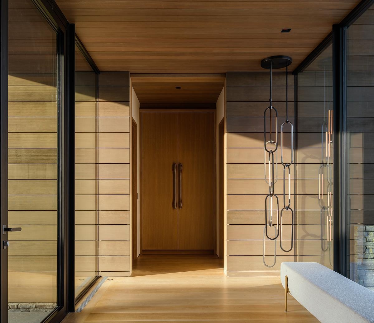 A floating bridge suspended above a dry creek bed creates a dramatic arrival experience, leading into a home defined by exposed timber, steel, stone, and breathtaking valley views.