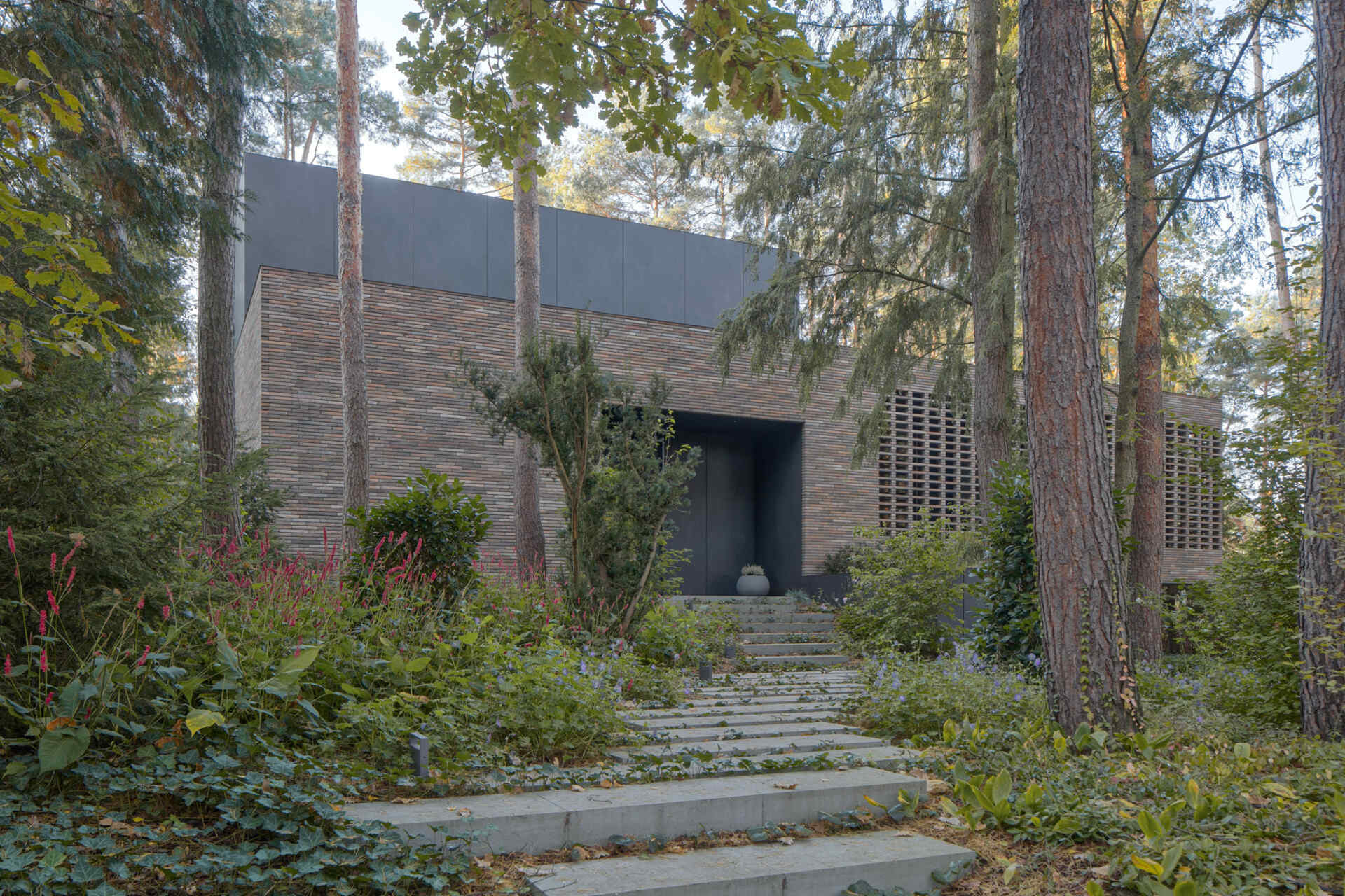 House with a Glade near Warsaw, Poland uses curved architecture, brick, glass, and graphite cladding to create a villa that seems to emerge from the surrounding pine forest.