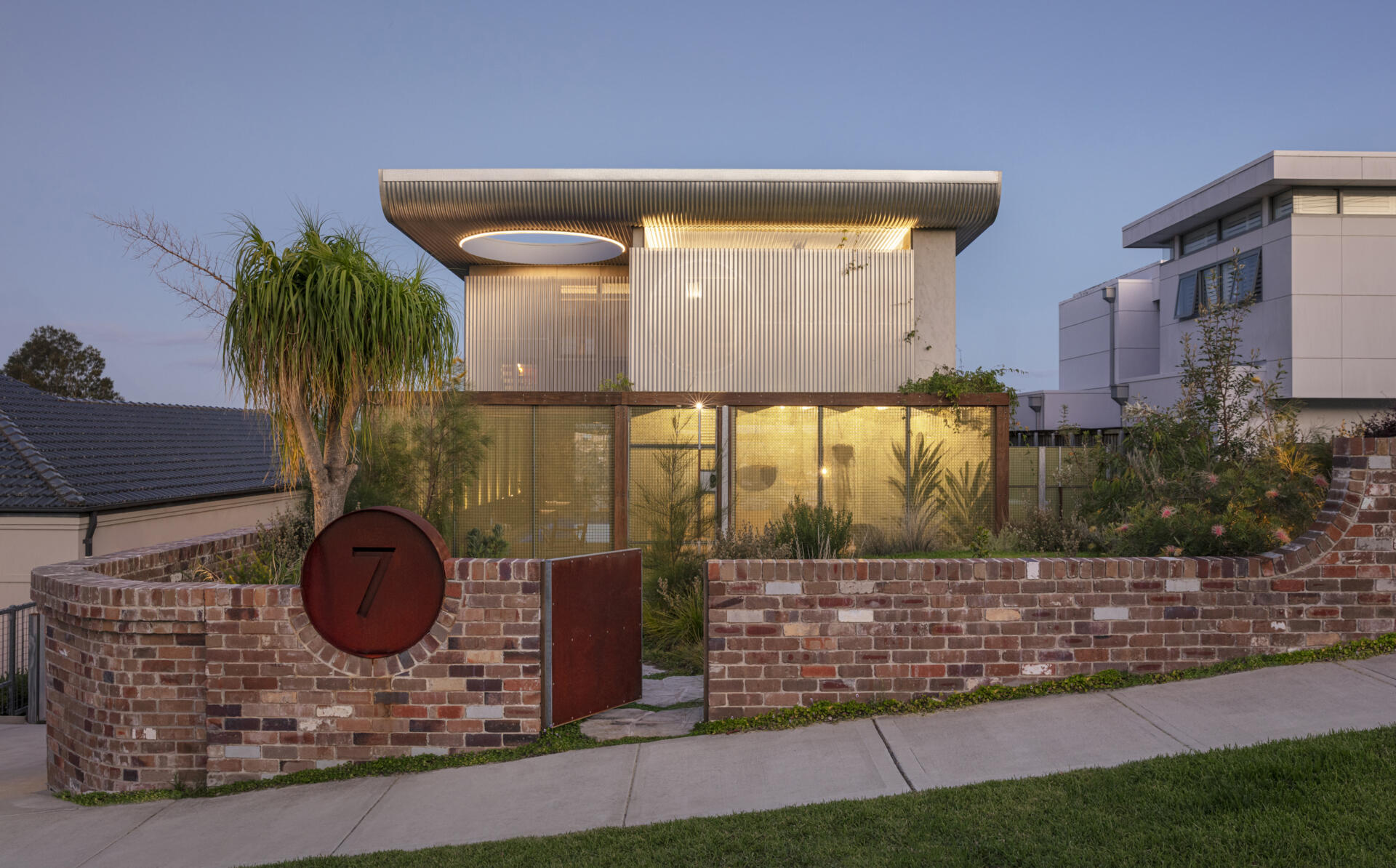 A stunning Sydney home featuring a dramatic butterfly roof, circular windows, curved brickwork, and translucent jade-green screens that create privacy without blocking light.