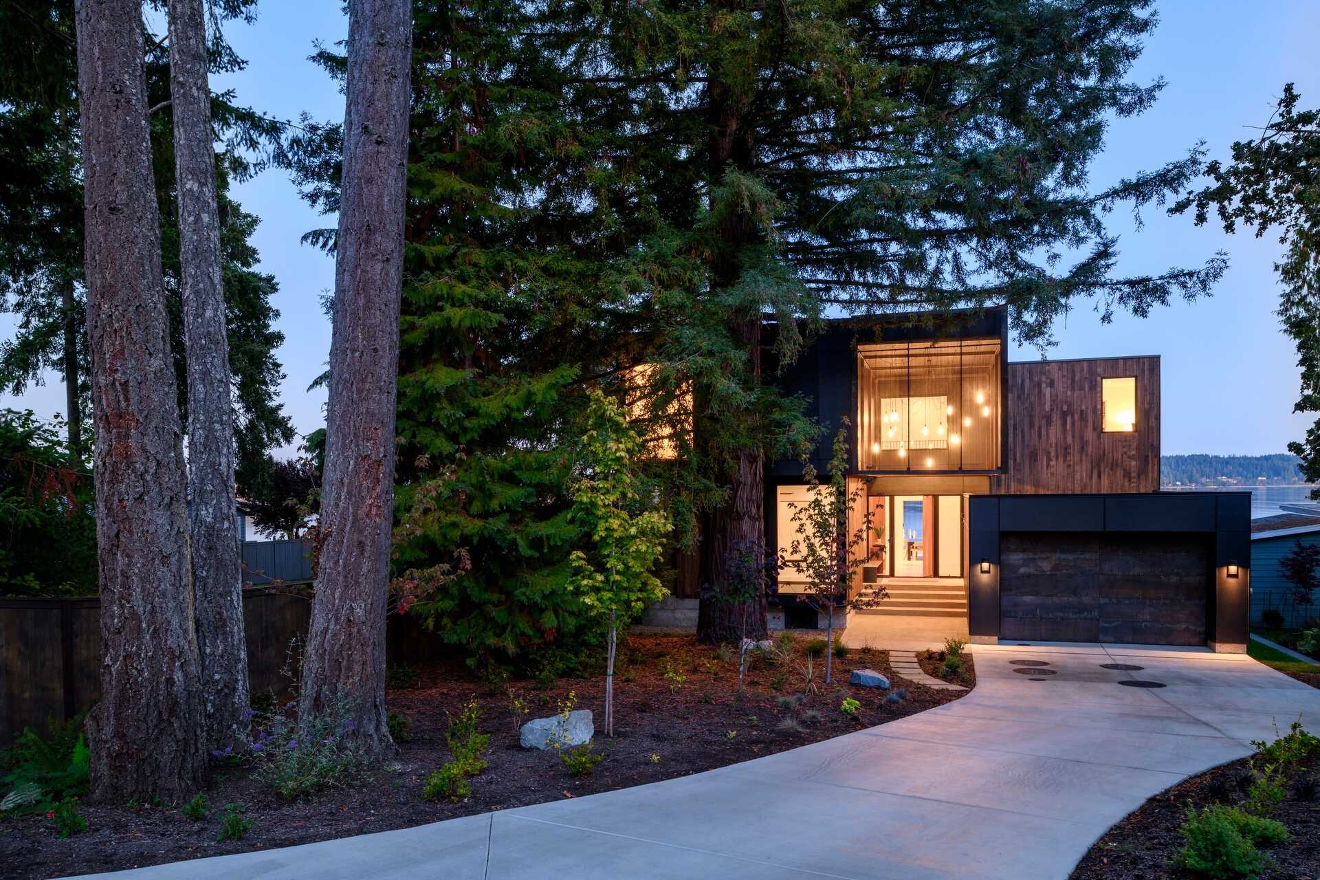 Framed by the island's oldest redwood tree, suspended lanterns welcome visitors, while a perforated steel scrim softens their glow as daylight fades.

Inside, the double-height entry continues the experience with a skylight above that fills the interior with natural light throughout the day.