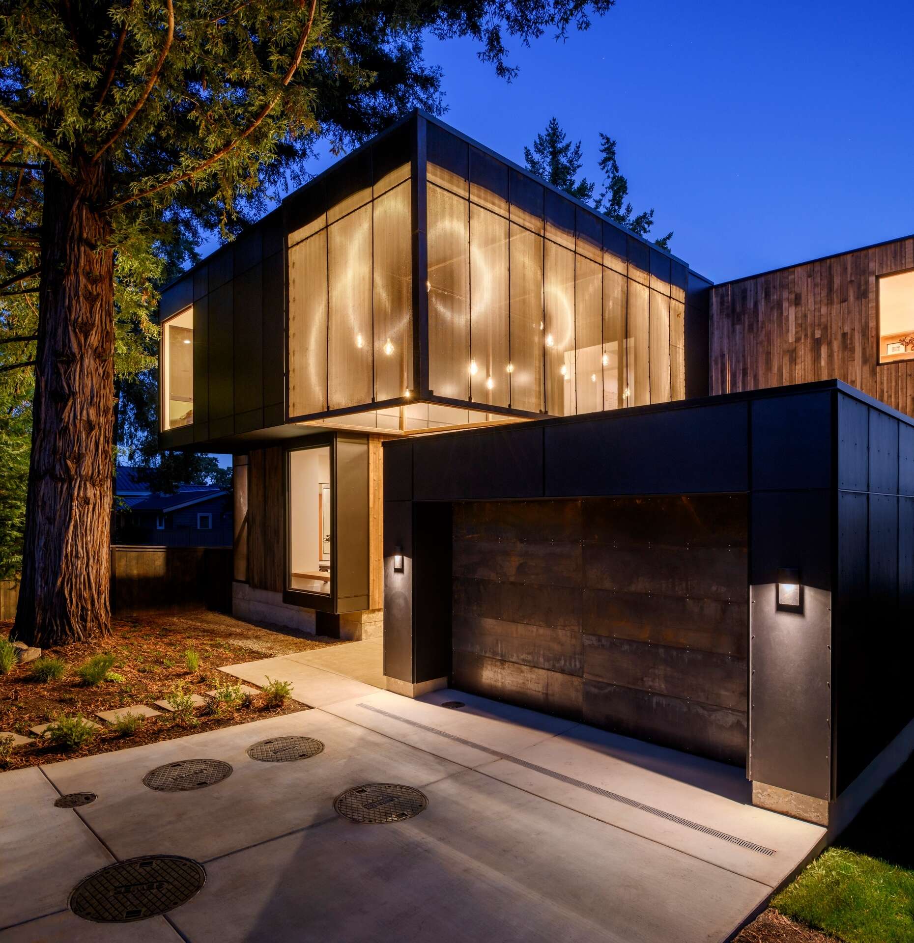 Framed by the island's oldest redwood tree, suspended lanterns welcome visitors, while a perforated steel scrim softens their glow as daylight fades.

Inside, the double-height entry continues the experience with a skylight above that fills the interior with natural light throughout the day.