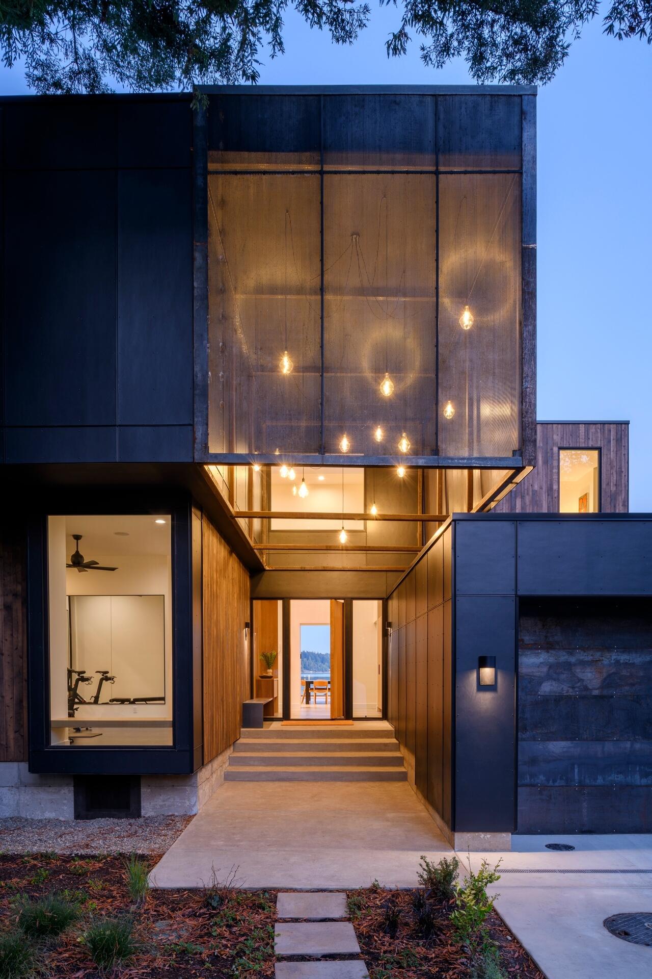 Framed by the island's oldest redwood tree, suspended lanterns welcome visitors, while a perforated steel scrim softens their glow as daylight fades.

Inside, the double-height entry continues the experience with a skylight above that fills the interior with natural light throughout the day.
