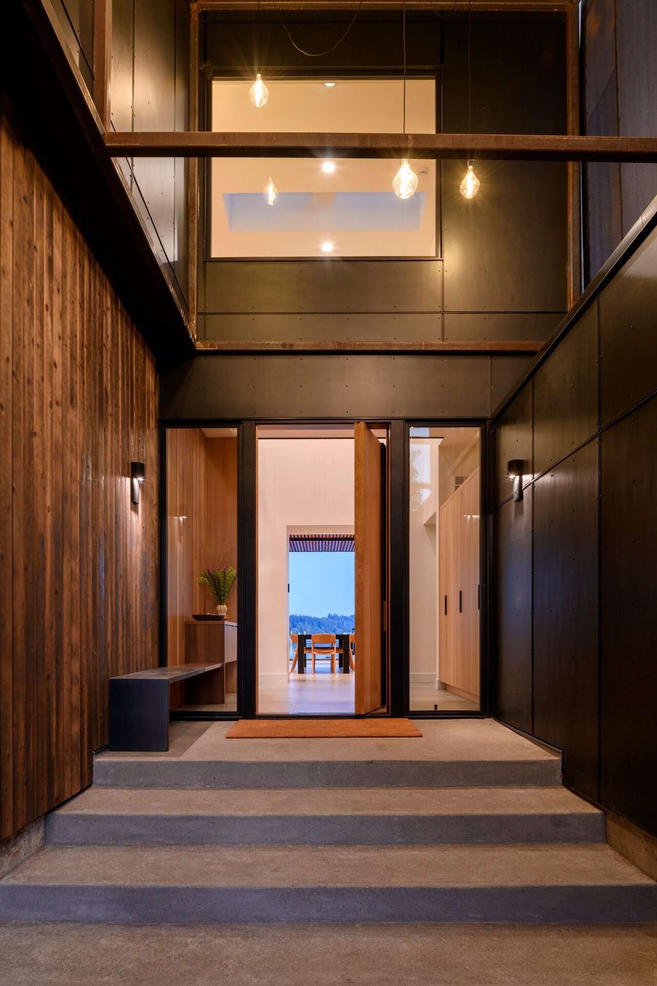 Framed by the island's oldest redwood tree, suspended lanterns welcome visitors, while a perforated steel scrim softens their glow as daylight fades.

Inside, the double-height entry continues the experience with a skylight above that fills the interior with natural light throughout the day.