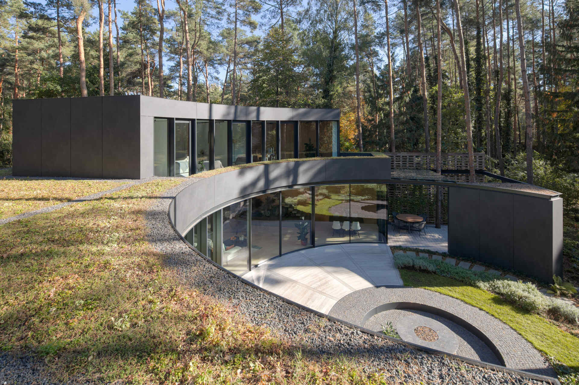 Curved upper-level glazing and planted roofs give House with a Glade its distinctive appearance. The combination of glass, greenery, and sweeping forms creates a striking contemporary forest home.