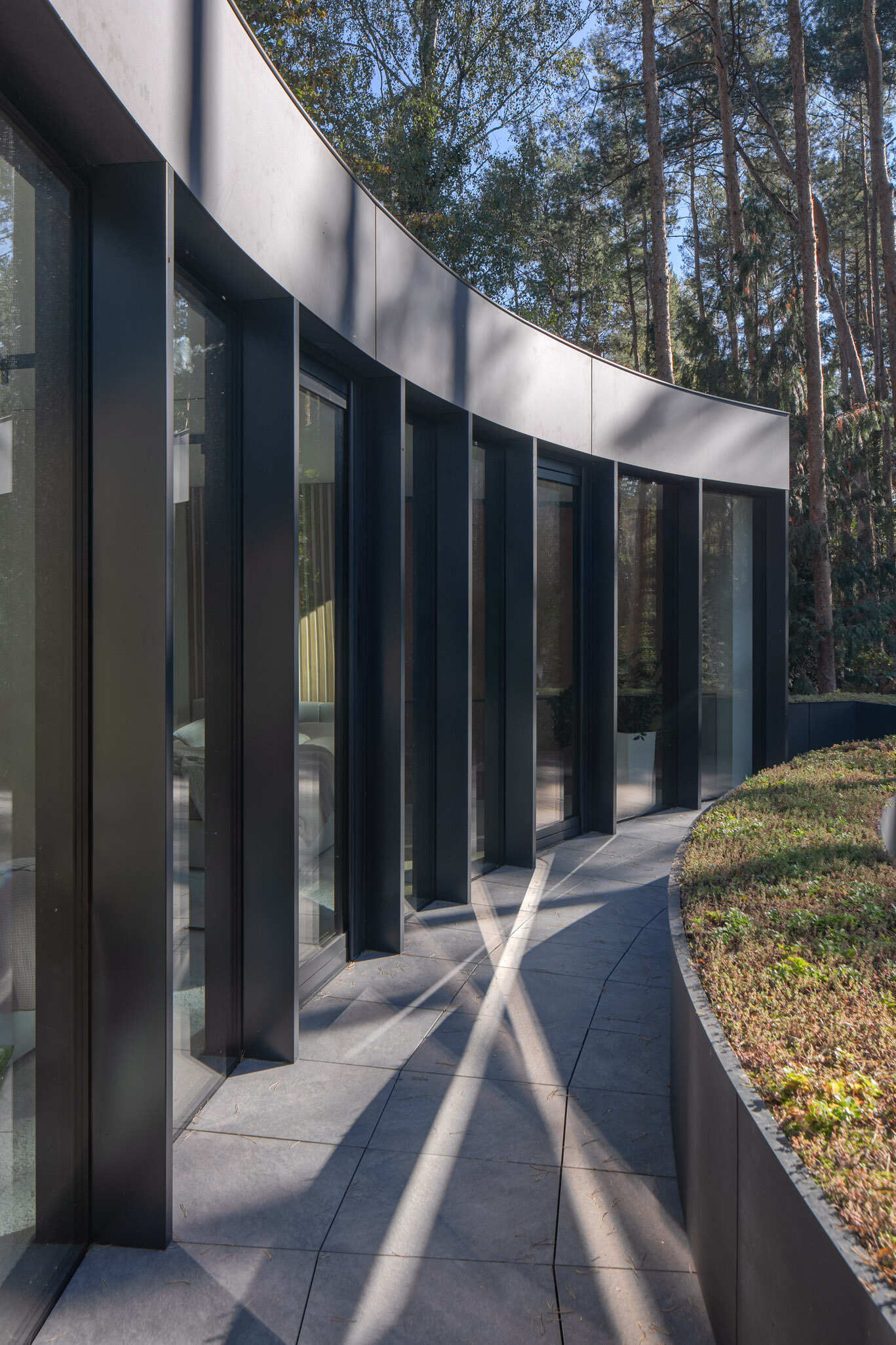 Curved upper-level glazing and planted roofs give House with a Glade its distinctive appearance. The combination of glass, greenery, and sweeping forms creates a striking contemporary forest home.