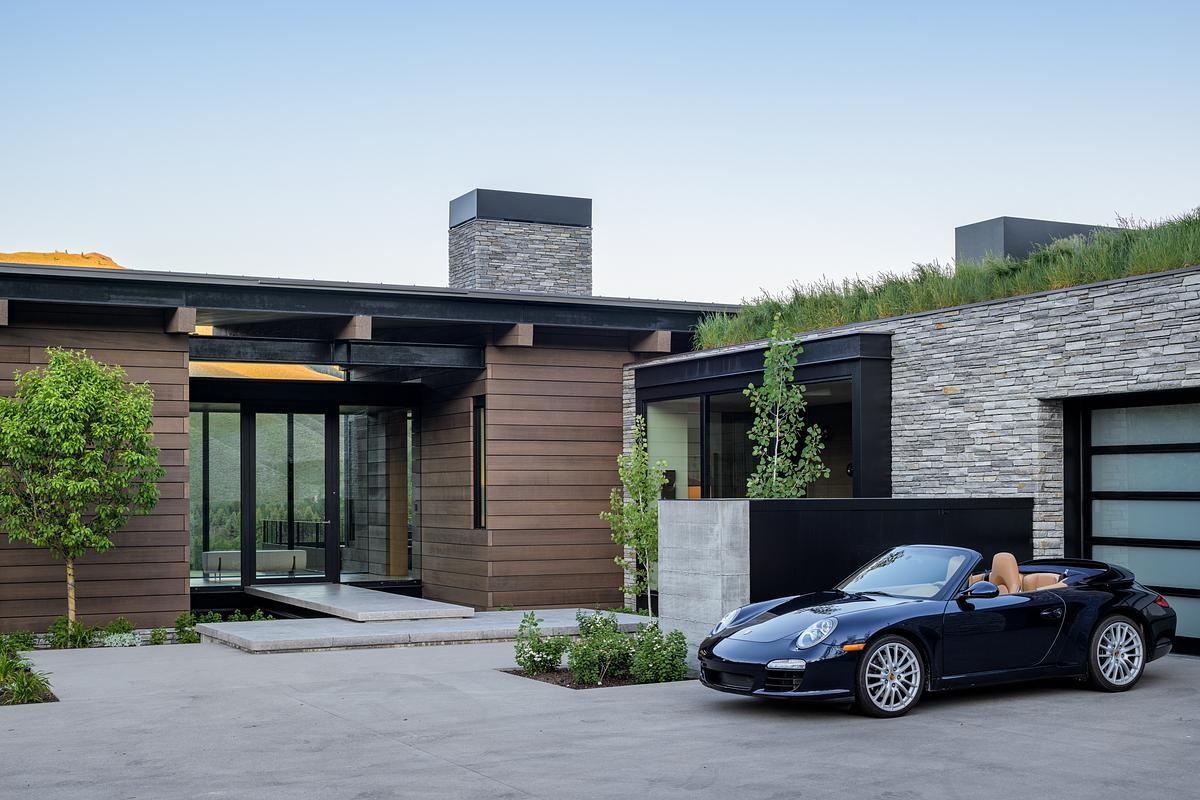 A floating bridge suspended above a dry creek bed creates a dramatic arrival experience, leading into a home defined by exposed timber, steel, stone, and breathtaking valley views.