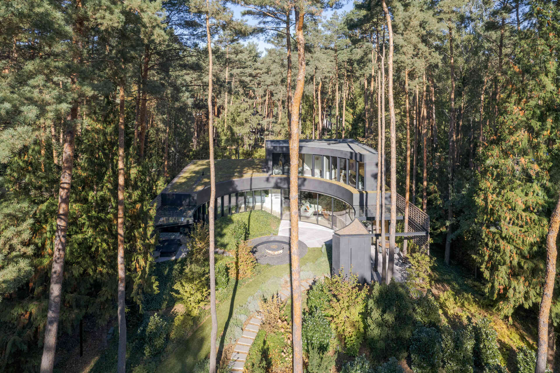 House with a Glade near Warsaw, Poland uses curved architecture, brick, glass, and graphite cladding to create a villa that seems to emerge from the surrounding pine forest.