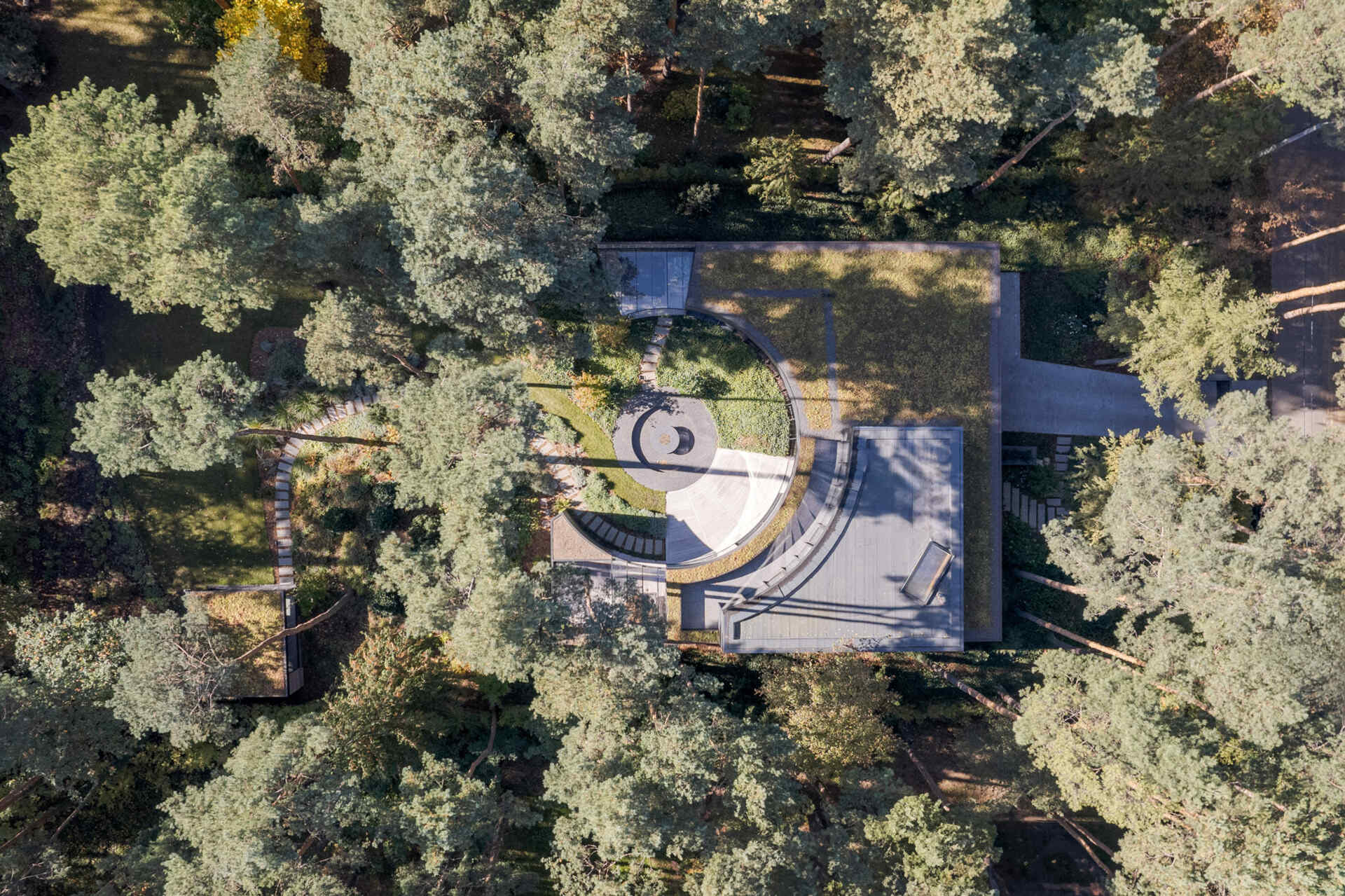 An aerial view of House with a Glade reveals green roofs woven into the forest canopy. The planted roofscape helps the villa blend into the woodland while adding an extra layer of sustainable design.