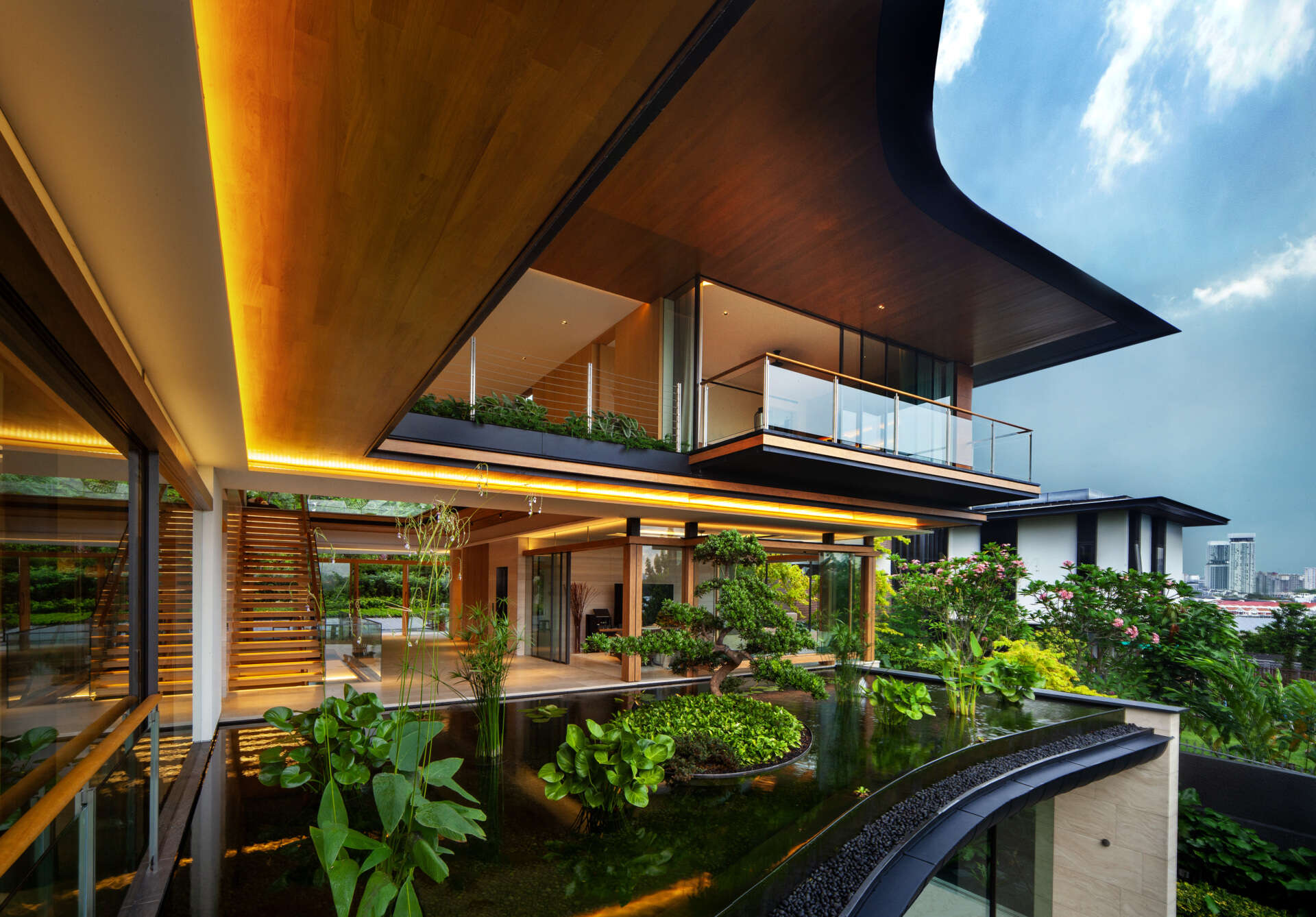 A multi-generational home filled with terraced gardens, rooftop lawns, reflecting ponds, and breathtaking city views. Warm timber interiors, tropical landscaping, open-air walkways, and a lagoon-like pool create a beautiful blend of architecture and nature.