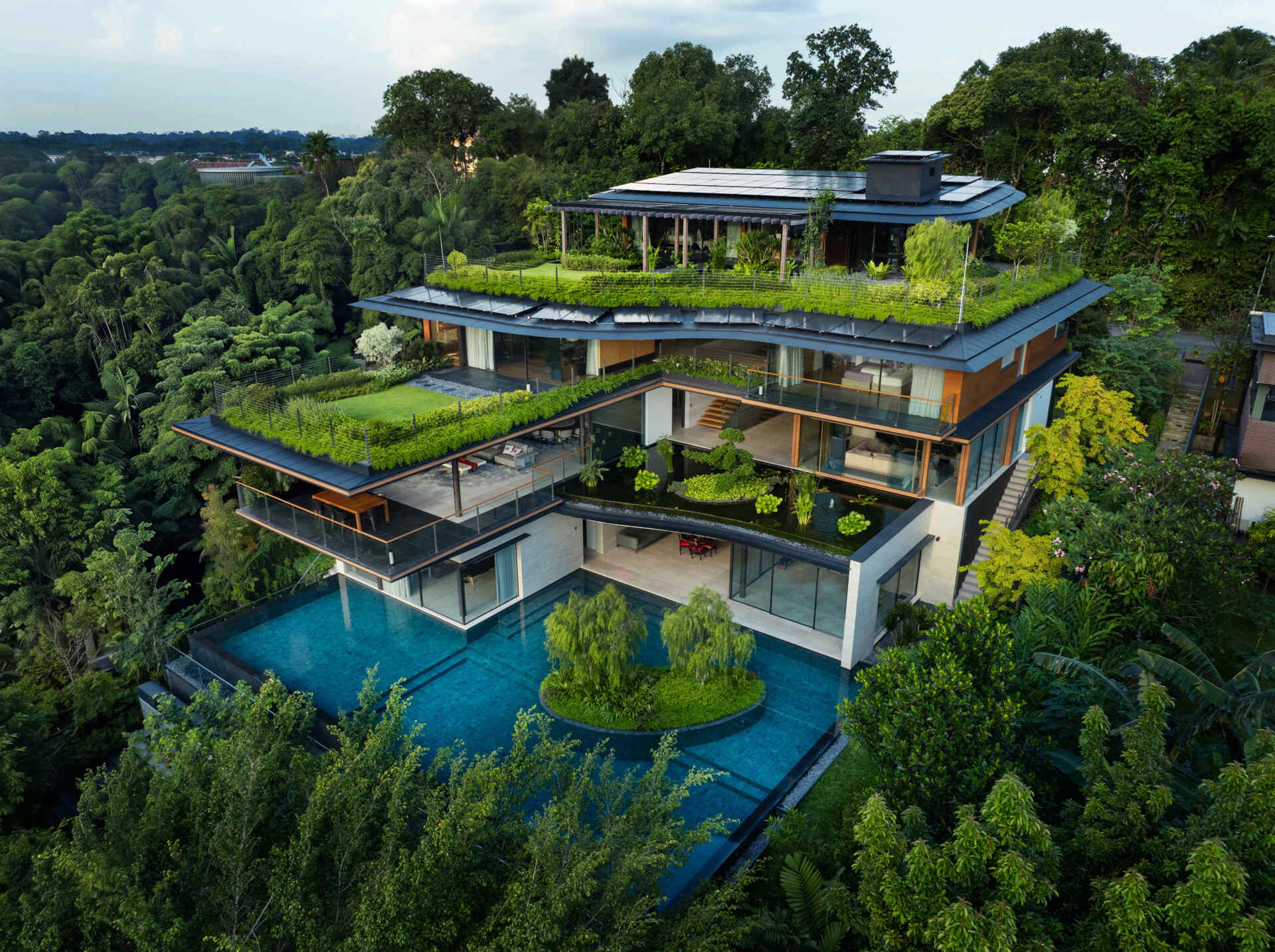 A multi-generational home filled with terraced gardens, rooftop lawns, reflecting ponds, and breathtaking city views. Warm timber interiors, tropical landscaping, open-air walkways, and a lagoon-like pool create a beautiful blend of architecture and nature.