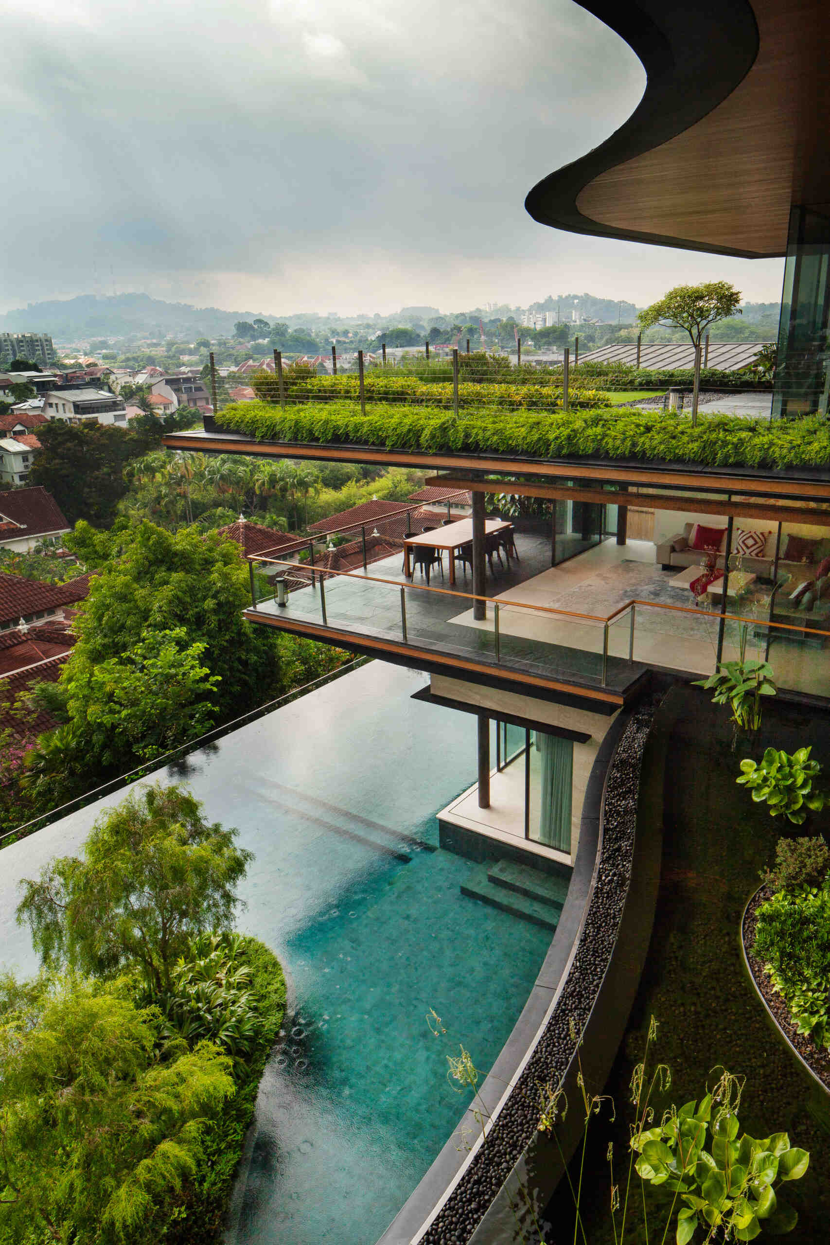 A multi-generational home filled with terraced gardens, rooftop lawns, reflecting ponds, and breathtaking city views. Warm timber interiors, tropical landscaping, open-air walkways, and a lagoon-like pool create a beautiful blend of architecture and nature.