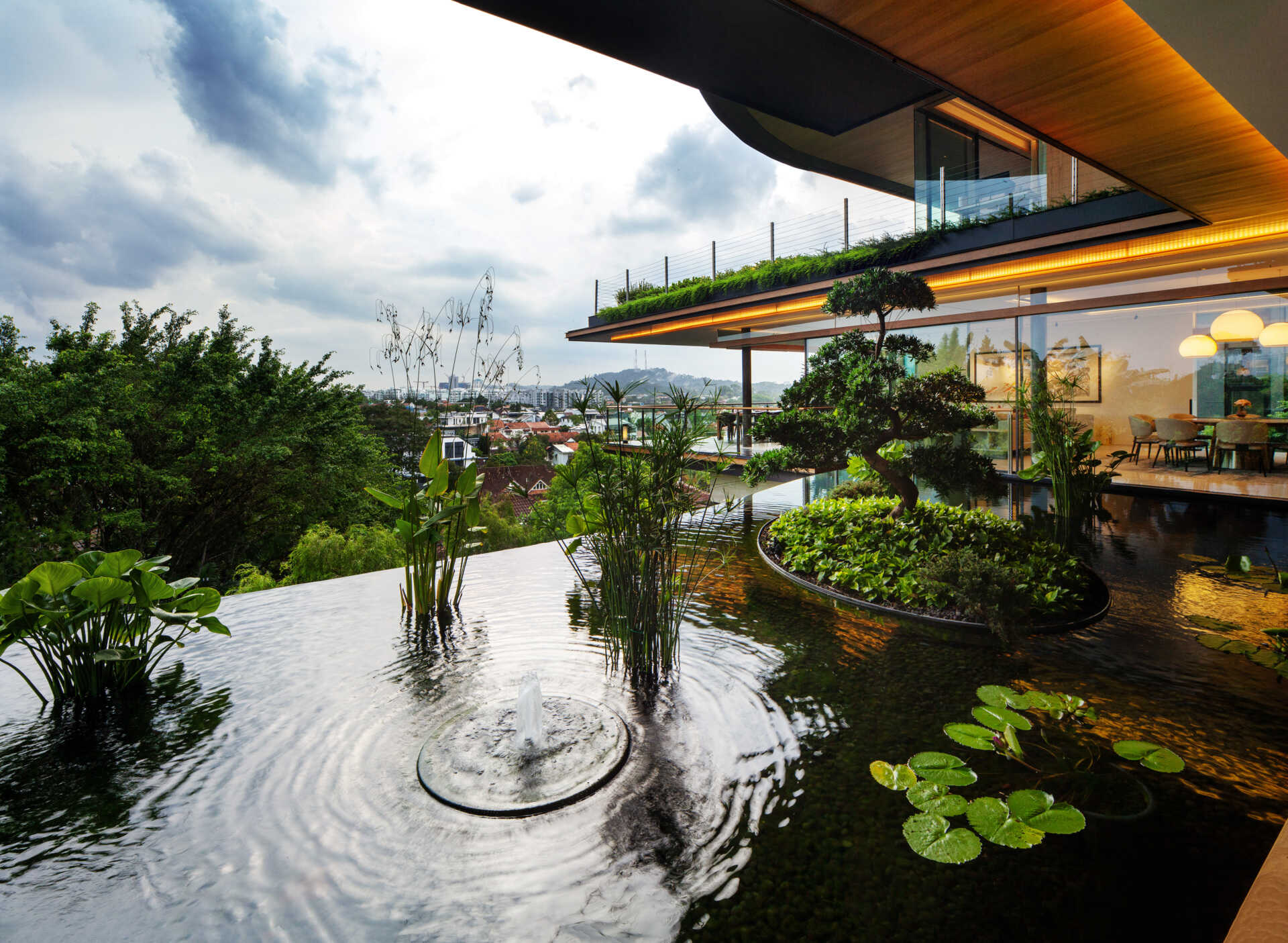 A multi-generational home filled with terraced gardens, rooftop lawns, reflecting ponds, and breathtaking city views. Warm timber interiors, tropical landscaping, open-air walkways, and a lagoon-like pool create a beautiful blend of architecture and nature.
