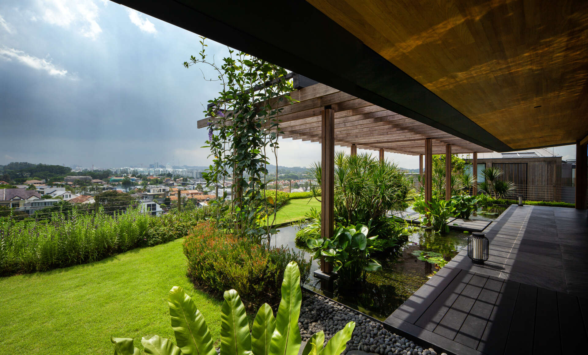 A multi-generational home filled with terraced gardens, rooftop lawns, reflecting ponds, and breathtaking city views. Warm timber interiors, tropical landscaping, open-air walkways, and a lagoon-like pool create a beautiful blend of architecture and nature.