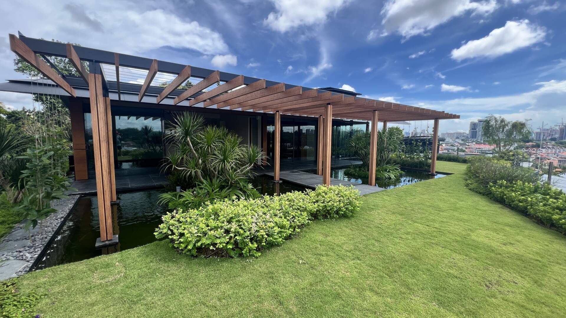 A multi-generational home filled with terraced gardens, rooftop lawns, reflecting ponds, and breathtaking city views. Warm timber interiors, tropical landscaping, open-air walkways, and a lagoon-like pool create a beautiful blend of architecture and nature.