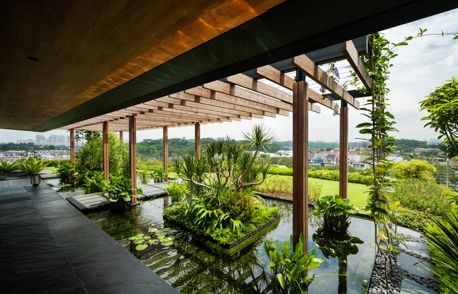 A multi-generational home filled with terraced gardens, rooftop lawns, reflecting ponds, and breathtaking city views. Warm timber interiors, tropical landscaping, open-air walkways, and a lagoon-like pool create a beautiful blend of architecture and nature.