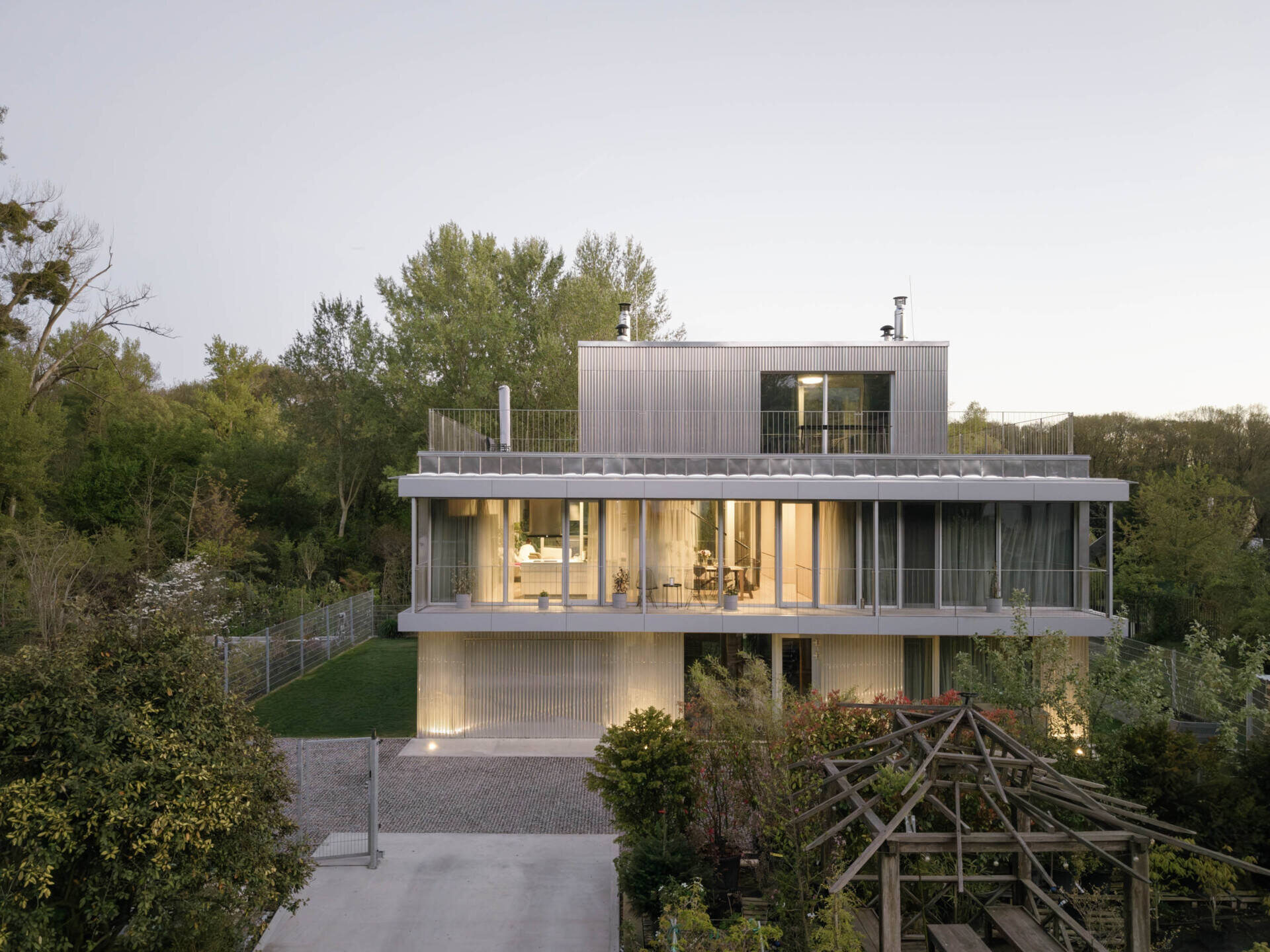 Set between the Carpathian foothills and the Danube River, this modern house features elevated living spaces, flexible interiors, panoramic views, a rooftop terrace, and a reflective raw aluminum facade that changes with the light throughout the day.