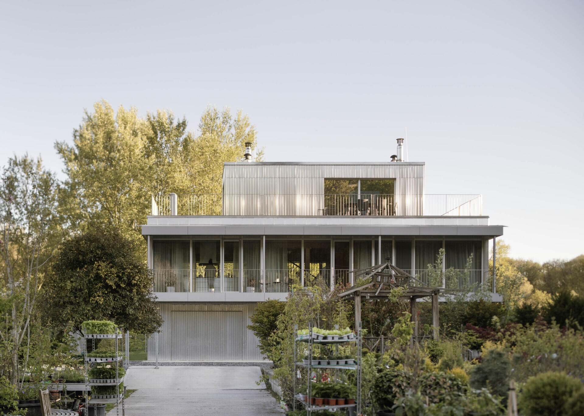 Set between the Carpathian foothills and the Danube River, this modern house features elevated living spaces, flexible interiors, panoramic views, a rooftop terrace, and a reflective raw aluminum facade that changes with the light throughout the day.