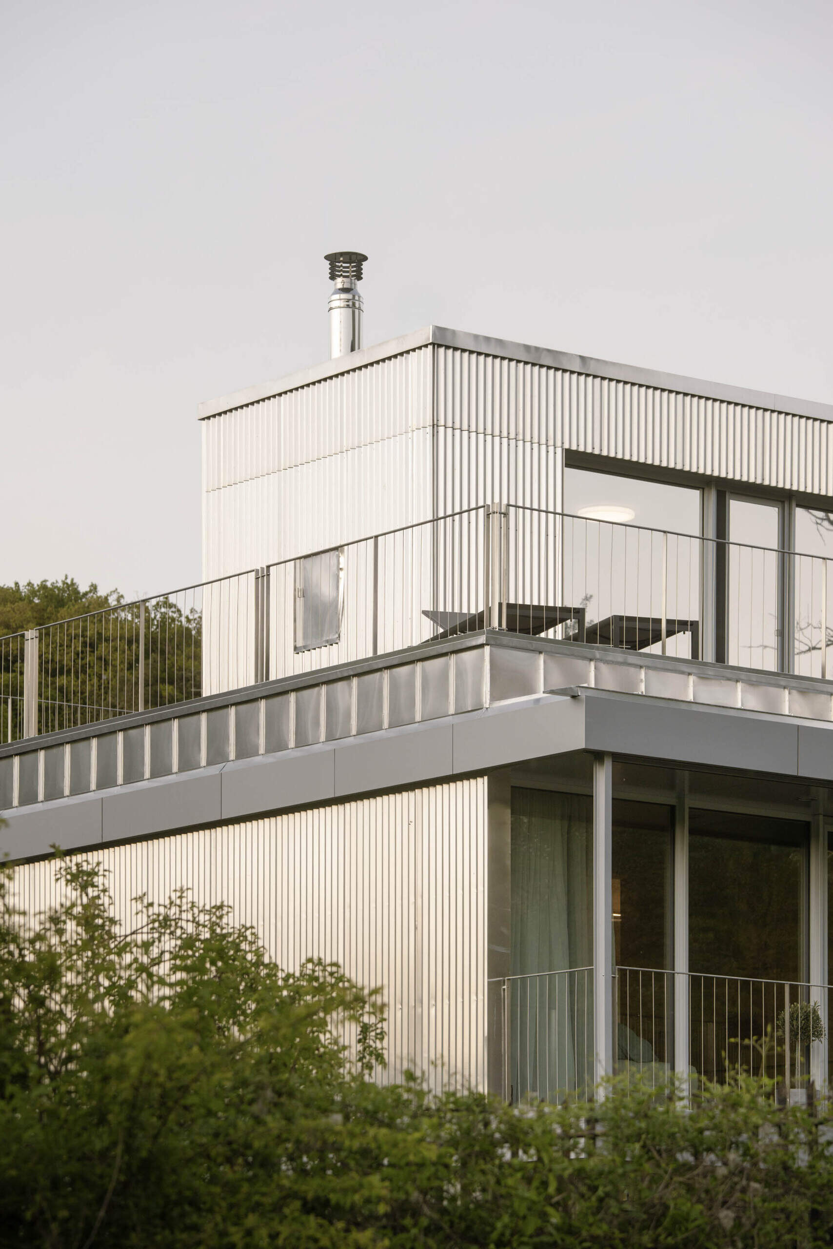 Set between the Carpathian foothills and the Danube River, this modern house features elevated living spaces, flexible interiors, panoramic views, a rooftop terrace, and a reflective raw aluminum facade that changes with the light throughout the day.